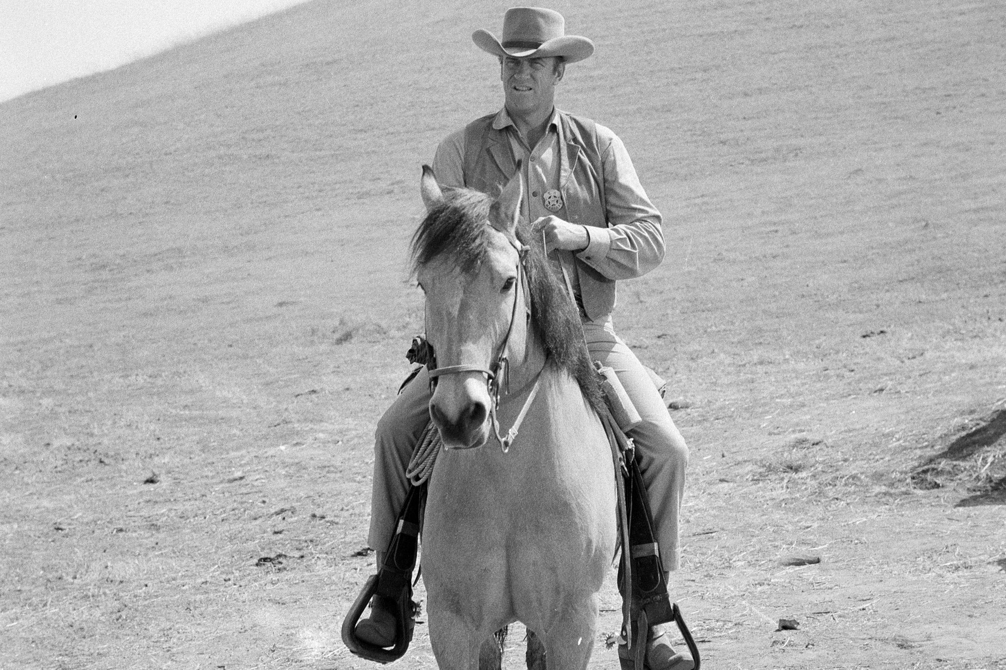 'Gunsmoke' James Arness as Matt Dillon riding a horse in a black-and-white picture