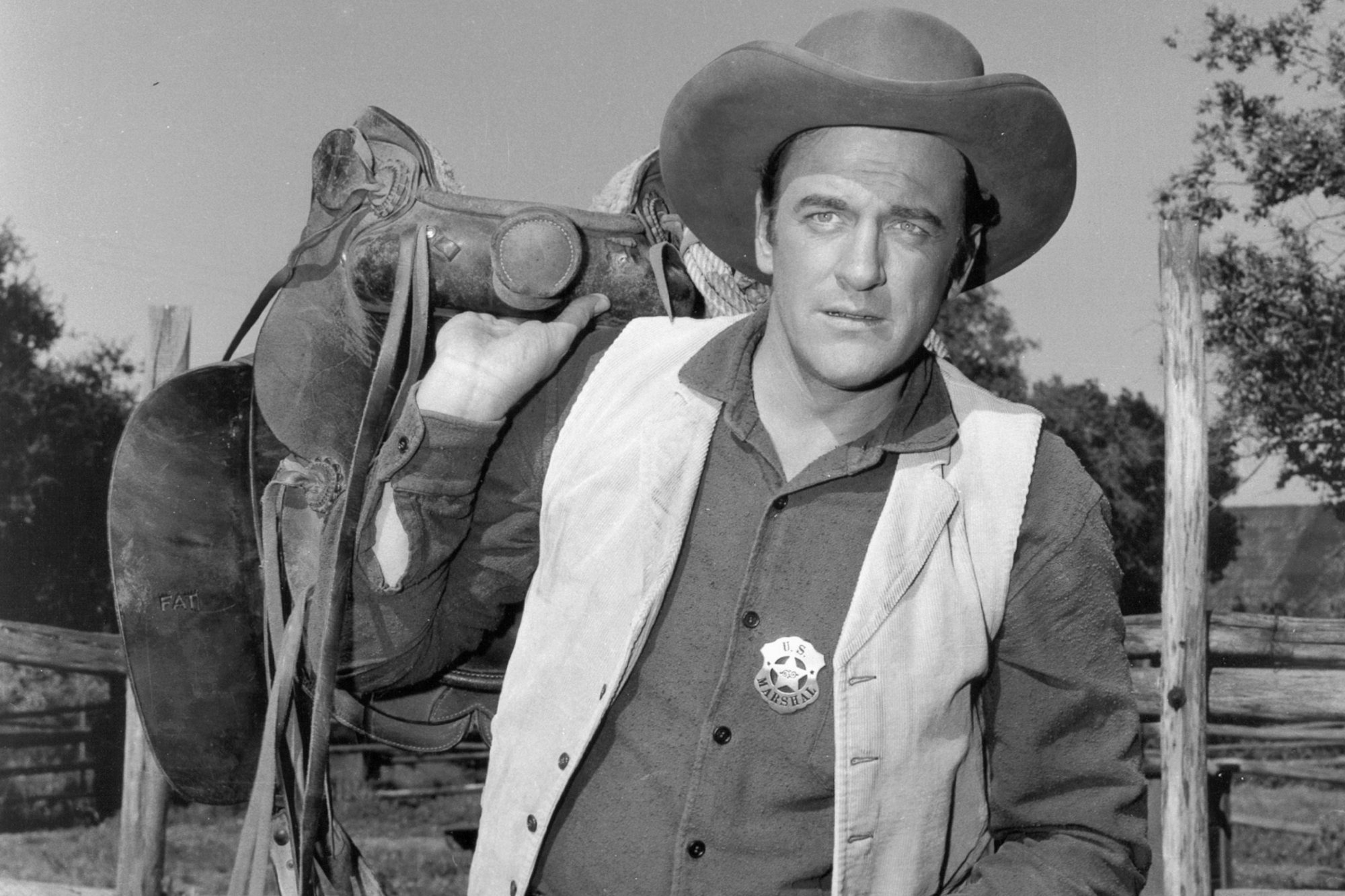 'Gunsmoke' James Arness as U.S. Marshal Matt Dillon in a black-and-white picture holding a horse saddle over his back