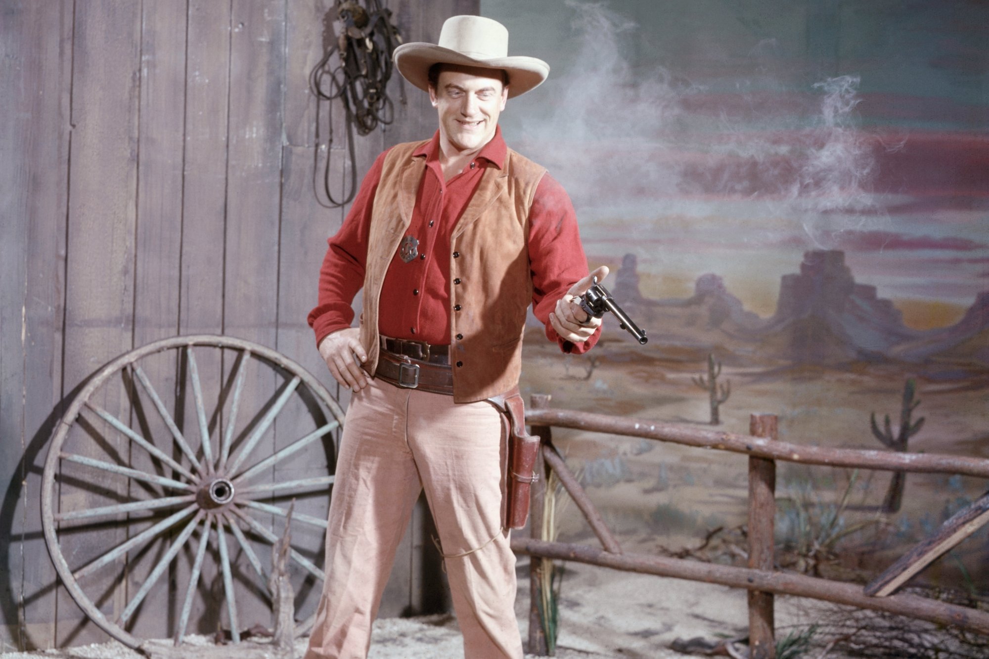 'Gunsmoke' James Arness as U.S. Marshal Matt Dillon wearing a Western outfit, holding out his pistol. He has a smile on his face.