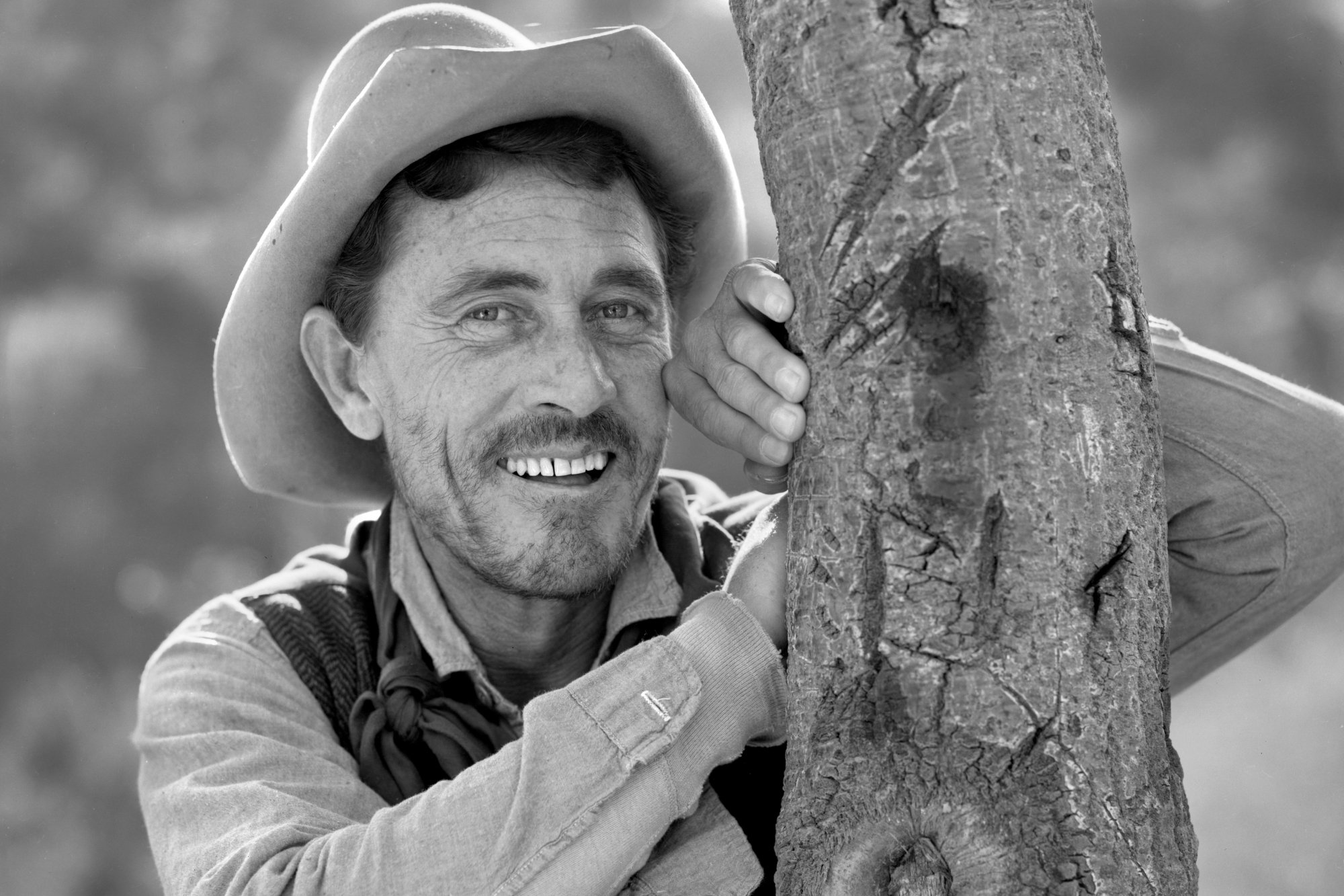 'Gunsmoke' Ken Curtis as Festus Haggen in a black-and-white picture smiling and leaning against a tree