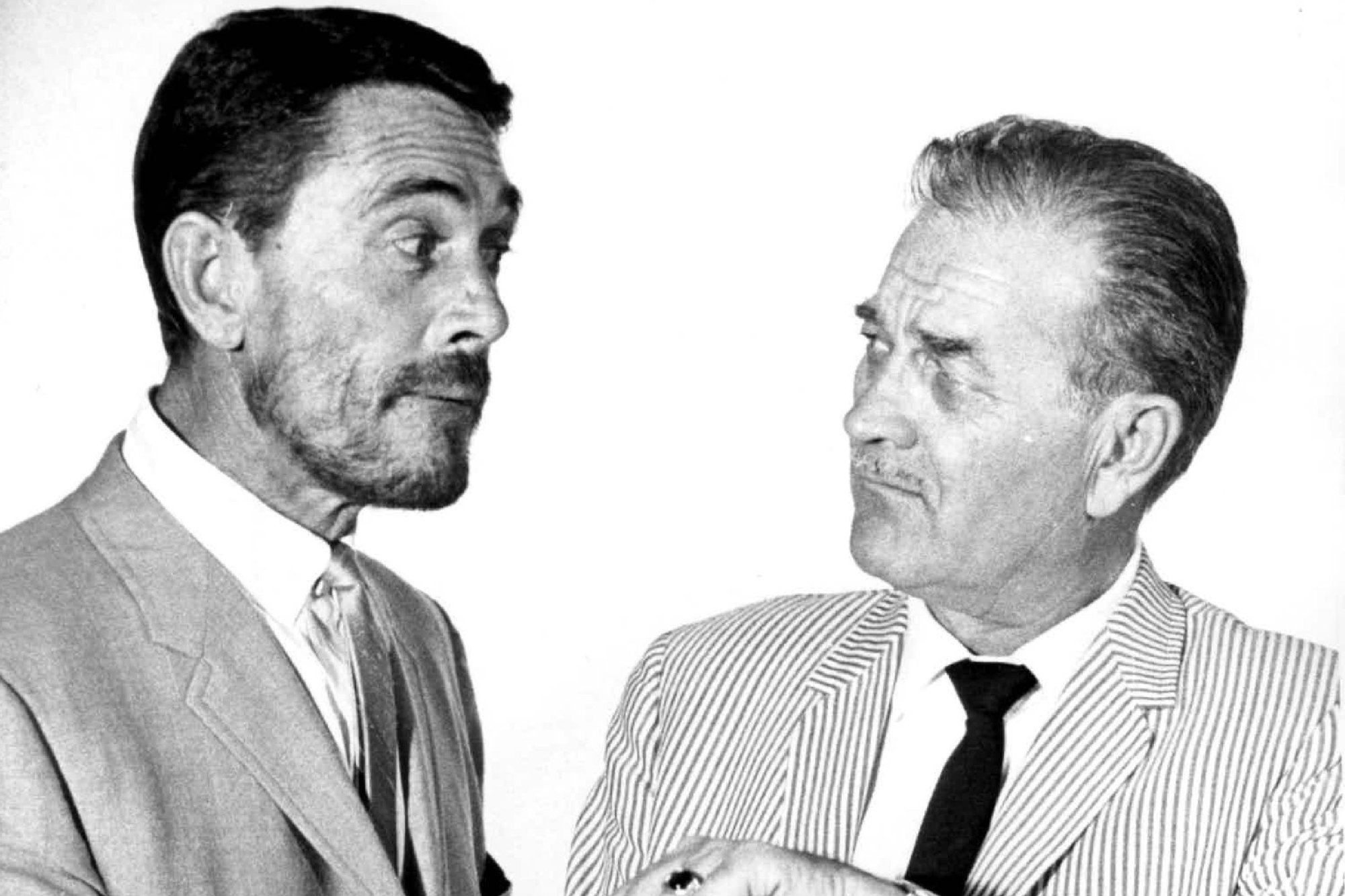 'Gunsmoke' actors Ken Curtis and Milburn Stone in a black-and-white picture giving exaggerated expressions to each other. They're both wearing suits and ties.