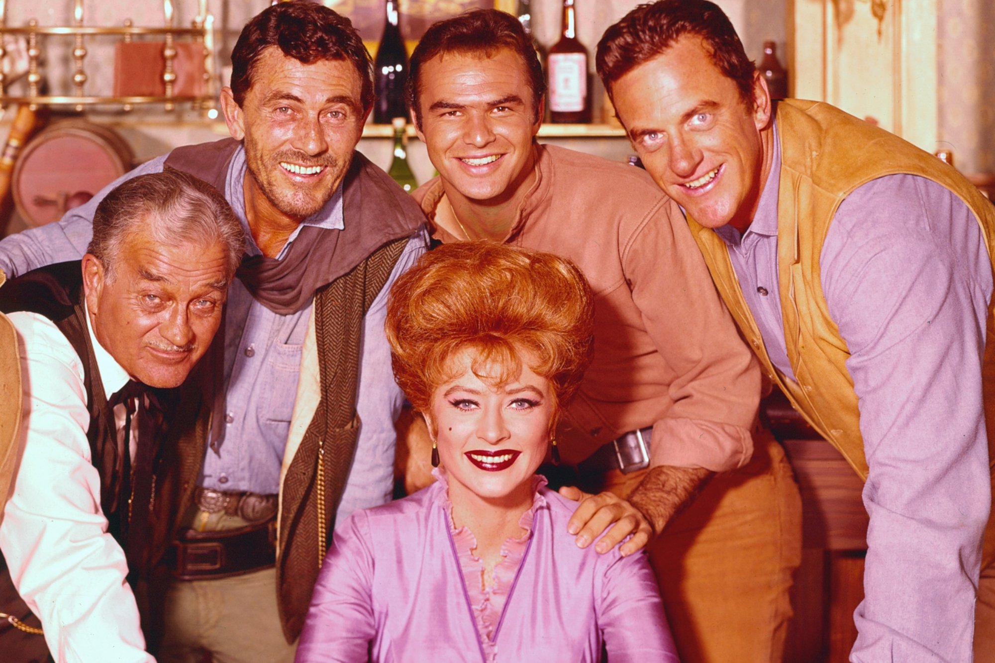 'Gunsmoke' net worth Milburn Stone as Doc Adams, Ken Curtis as Festus Haggen, Amanda Blake as Miss Kitty Russell, Burt Reynolds as Quint Asper, and James Arness as Matt Dillon in a publicity photo surrounding Blake, who is sitting down.