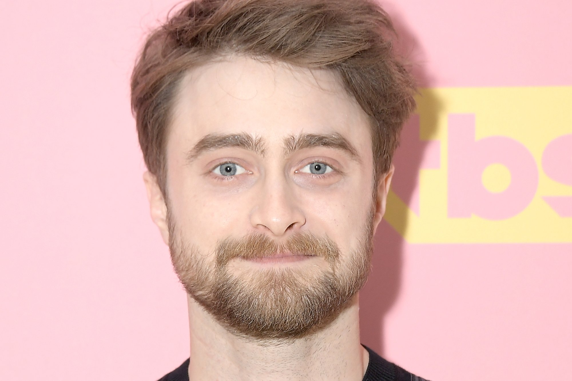 'Harry Potter' star Daniel Radcliffe with a closed-mouth smile on his face standing in front of a pink step and repeat