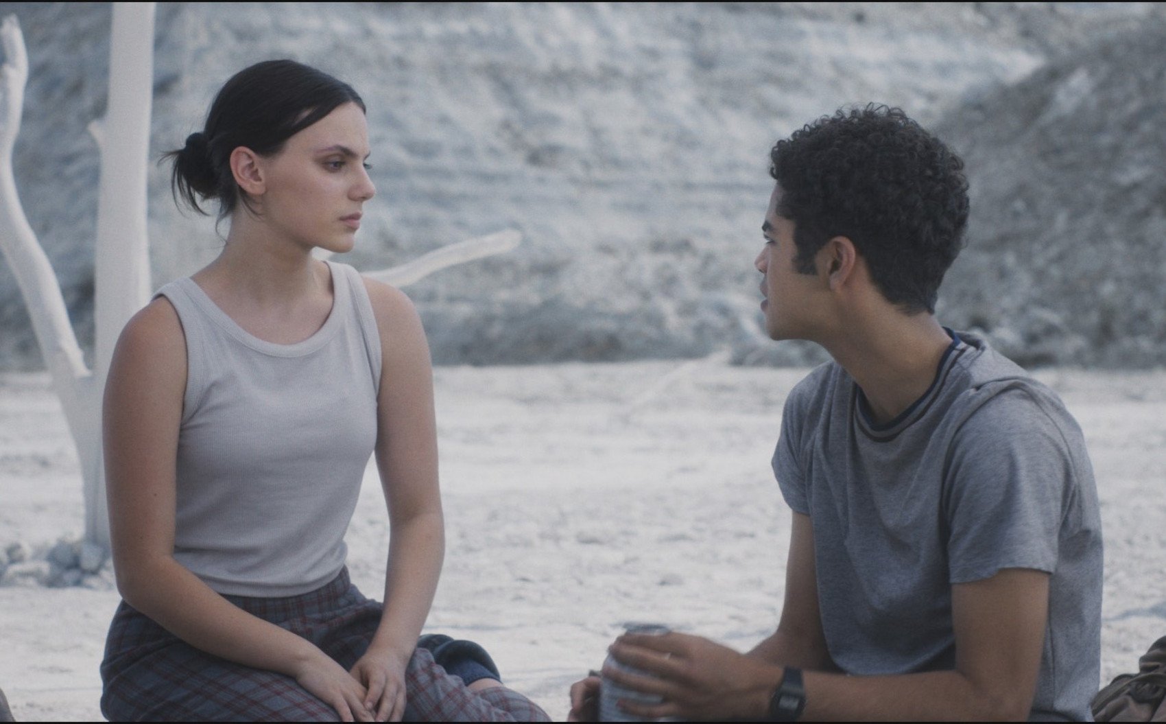 Dafne Keen and Amir Wilson as Lyra and Will in 'His Dark Materials' Season 3, Episode 3. They're sitting on sand and staring at one another.