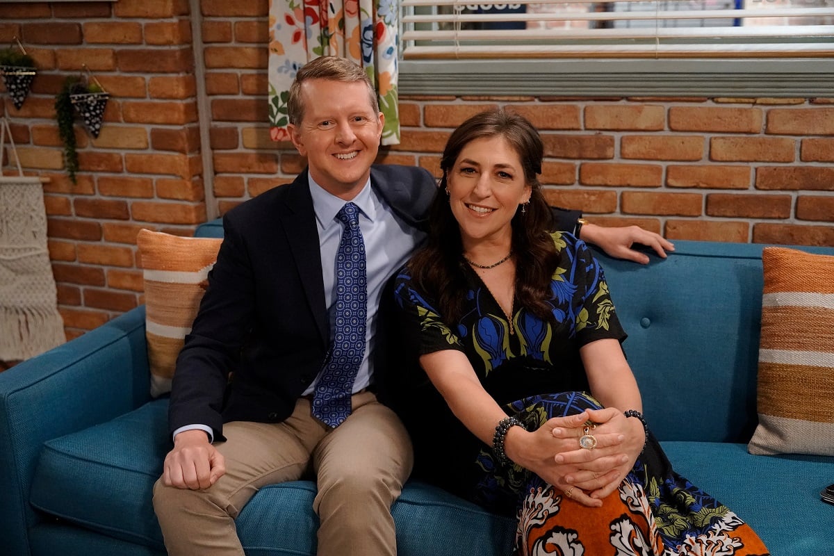 'Jeopardy!' hosts Ken Jennings and Mayim Bialik sitting on a couch on set of Bialik's sitcom 'Call Me Kat.'