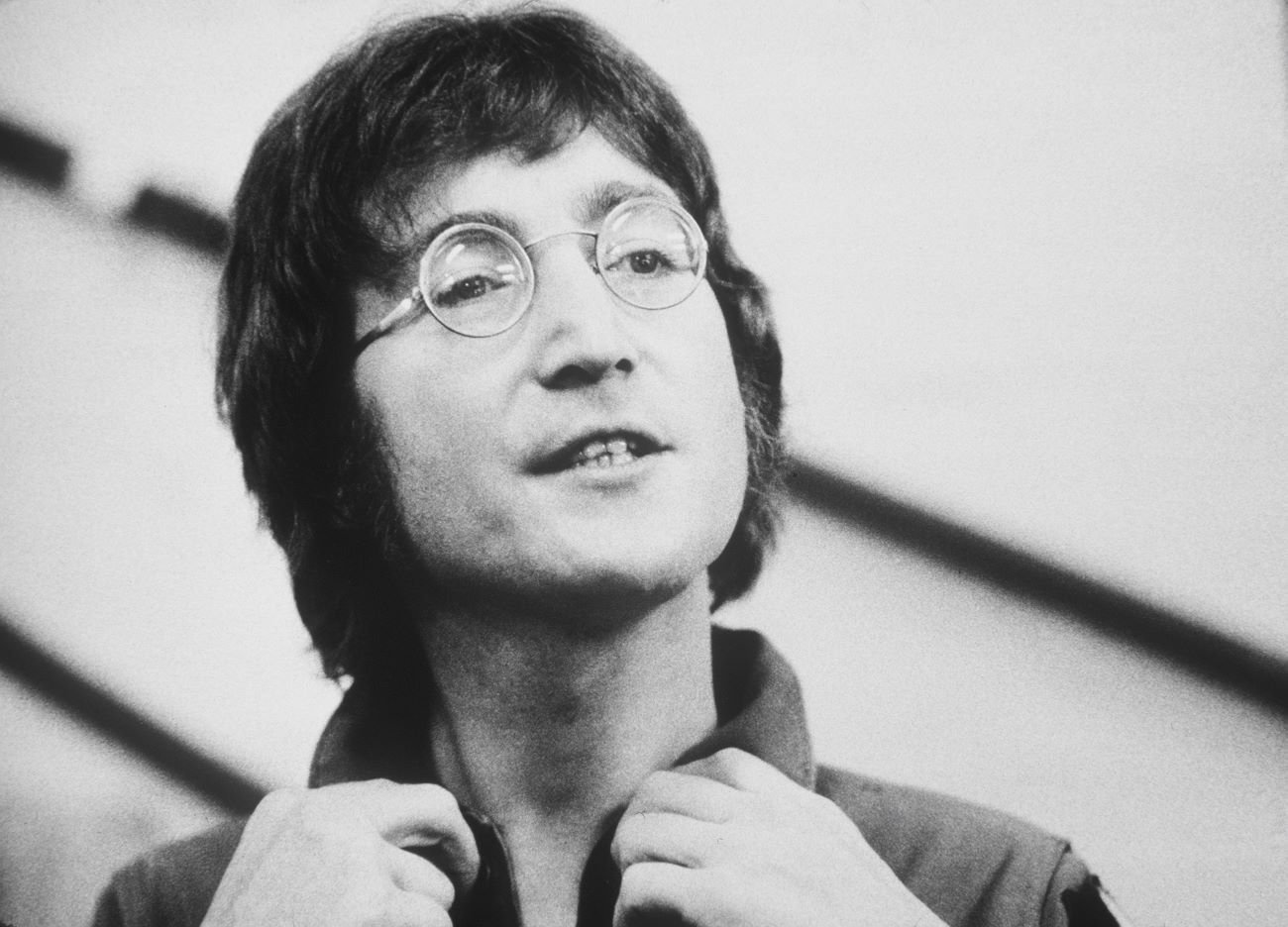 John Lennon wearing glasses and holding the collar of his shirt.