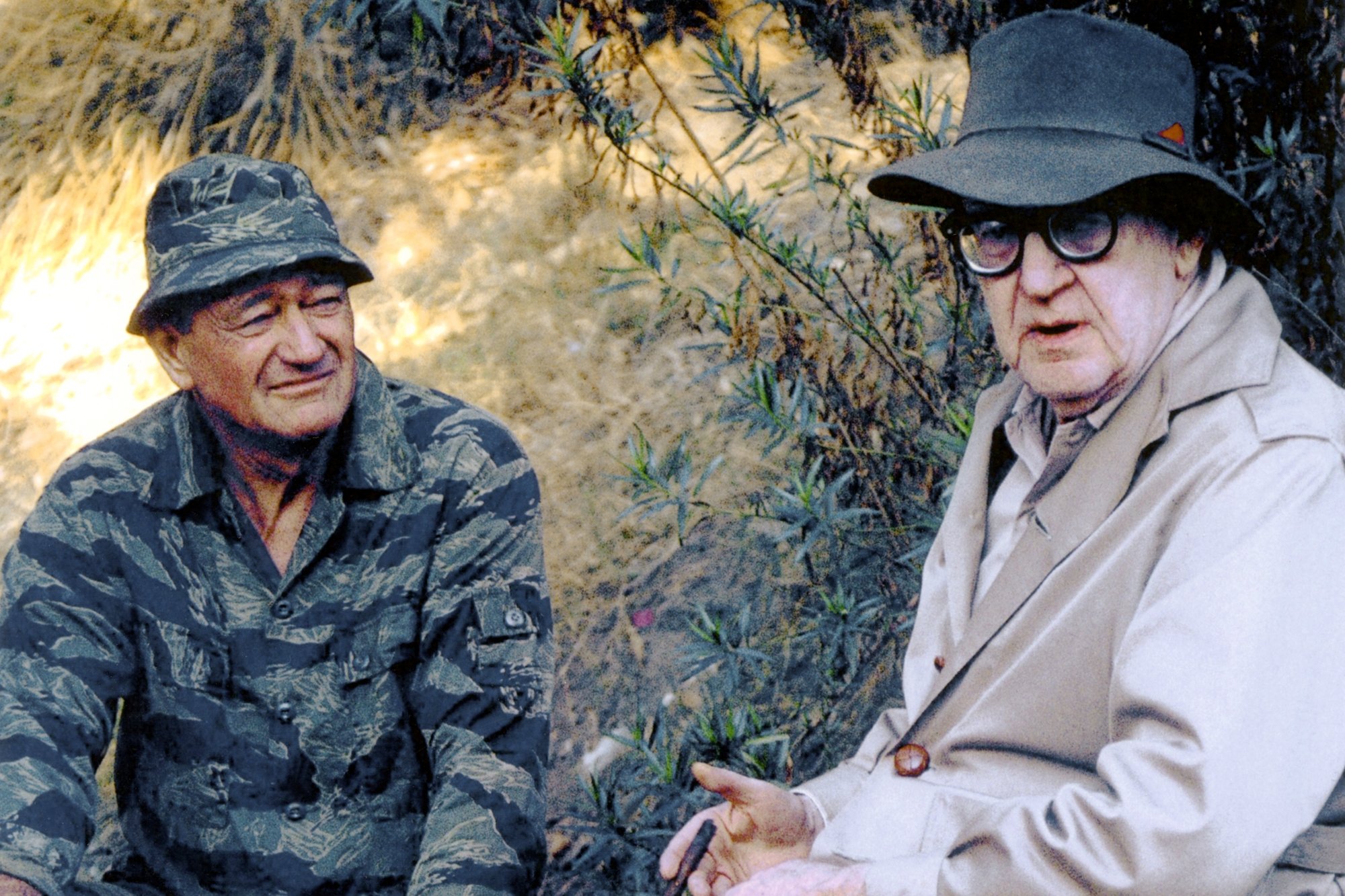 John Wayne and John Ford. Wayne is wearing an Army uniform and Wayne is wearing a hat looking at the camera.