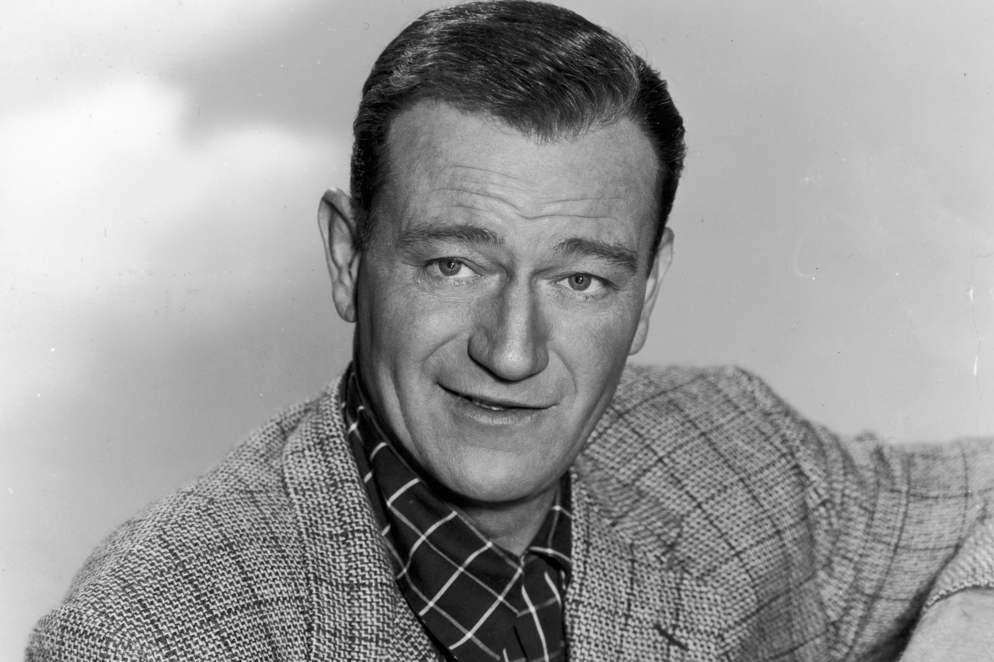 John Wayne, star of Western movies, in a black-and-white picture with a smile on his face.