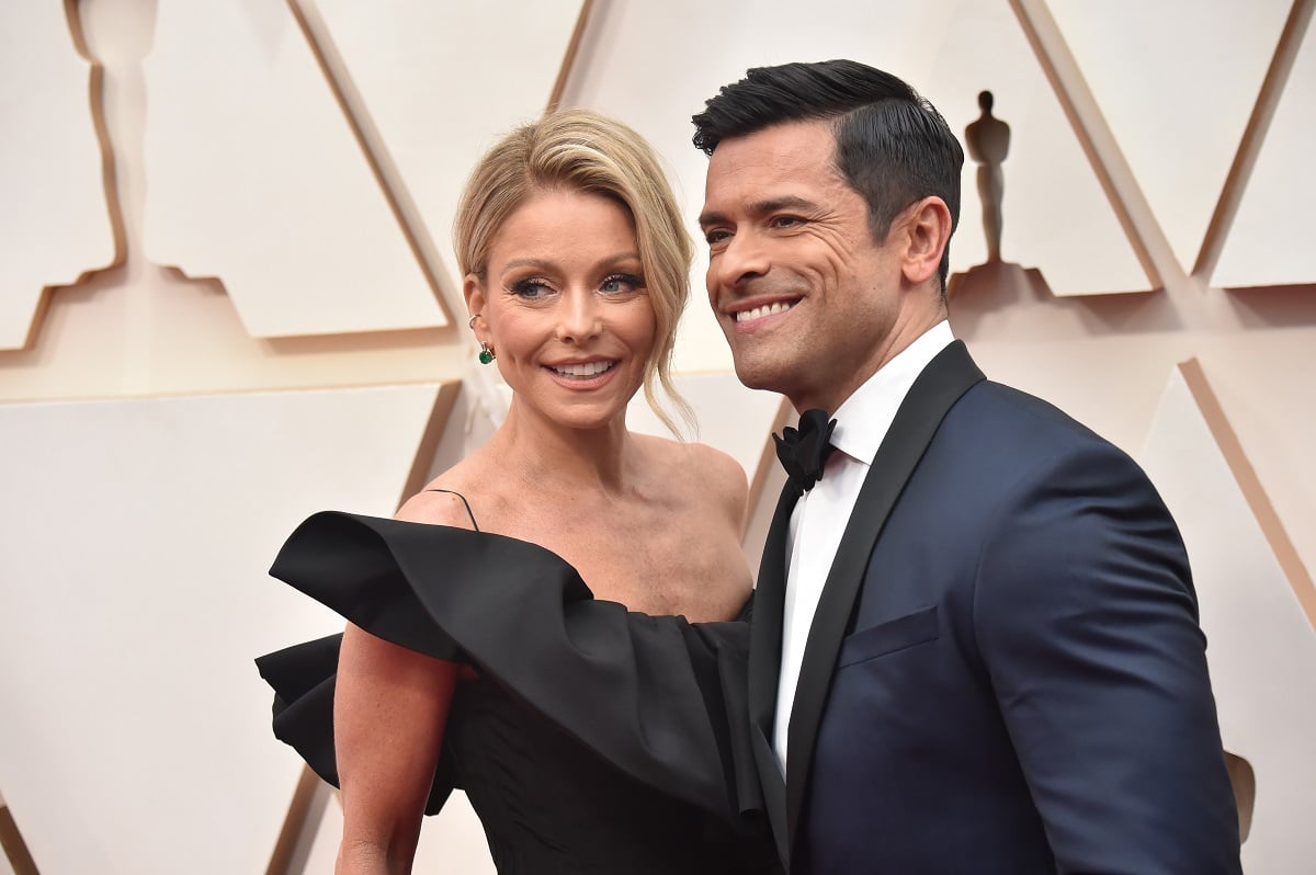 Kelly Ripa in a black dress and Mark Consuelos in a blue tuxedo smile for a photo on the Oscar red carpet.