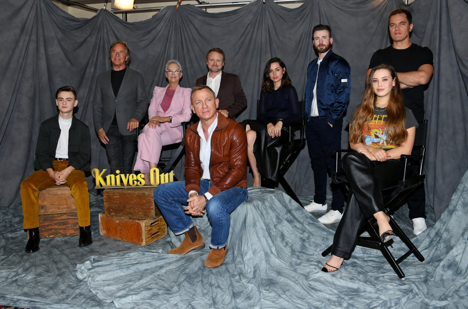 Jaeden Martell, Don Johnson, Jamie Lee Curtis, Rian Johnson, Daniel Craig, Chris Evans, Ana de Armas, Michael Shannon and Katherine Langford for our article about whether 'Knives Out' is on Netflix. They're posing next to a statue of the movie's logo.