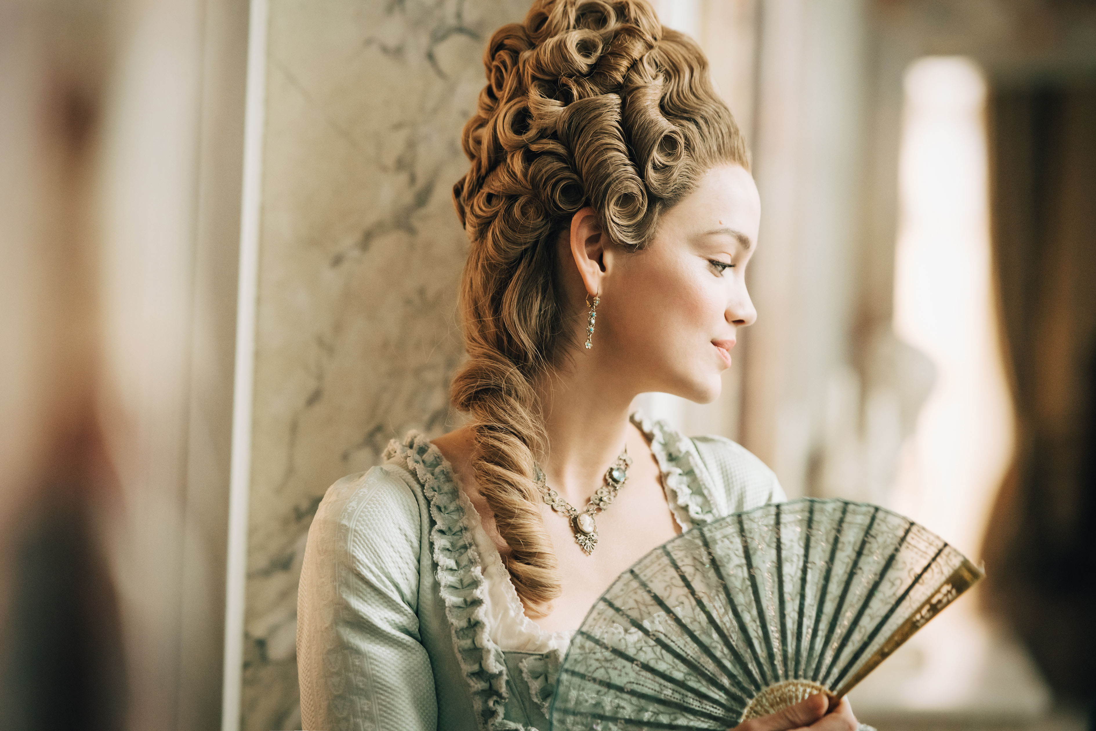 Emilia Schüle as Marie Antoinette, holding a fan, in the PBS series 'Marie Antoinette'