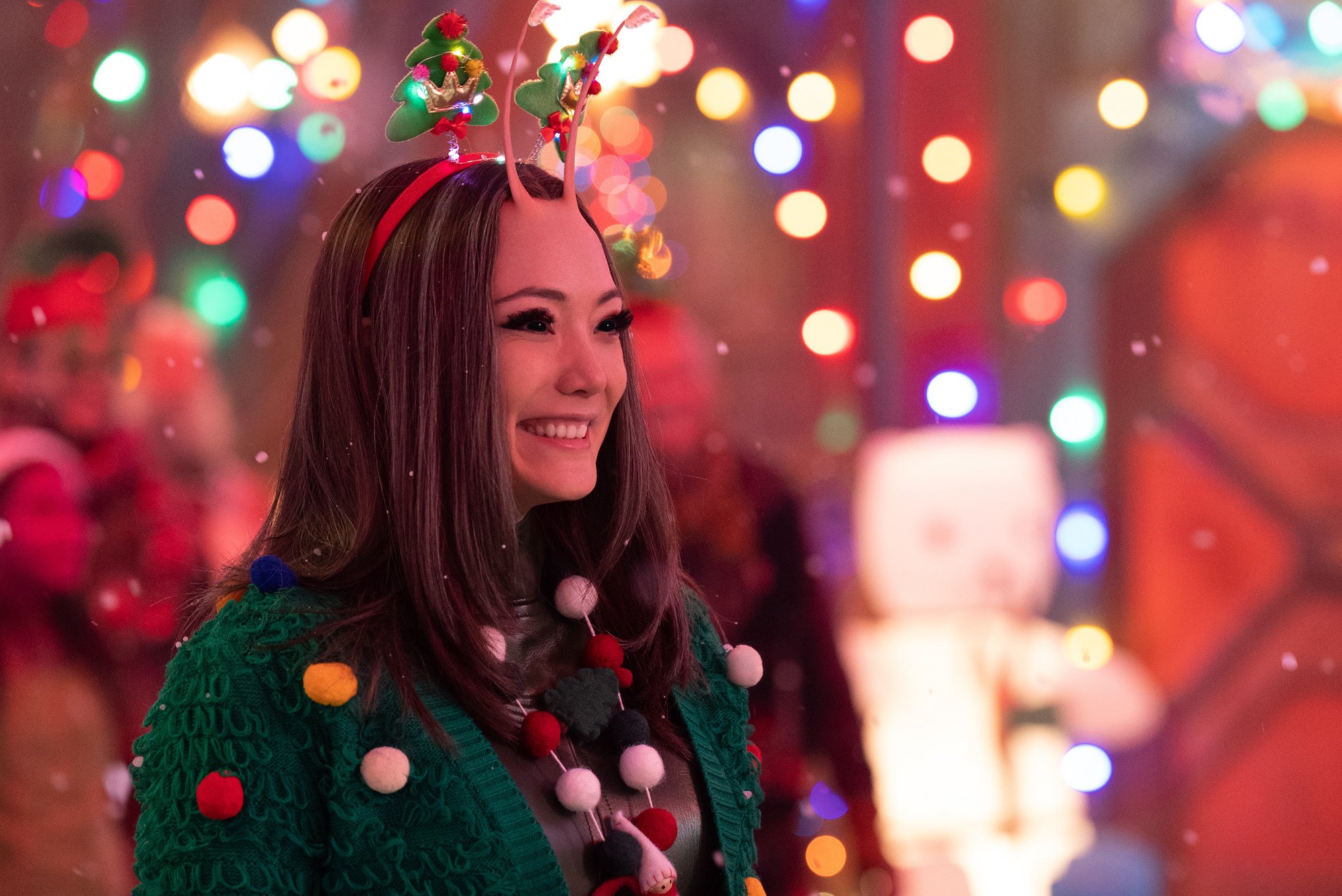 Pom Klementieff, as her Marvel character Mantis in 'The Guardians of the Galaxy Holiday Special' on Disney+ in 2022, wears a green holiday cardigan and a red headband with Christmas trees on top.