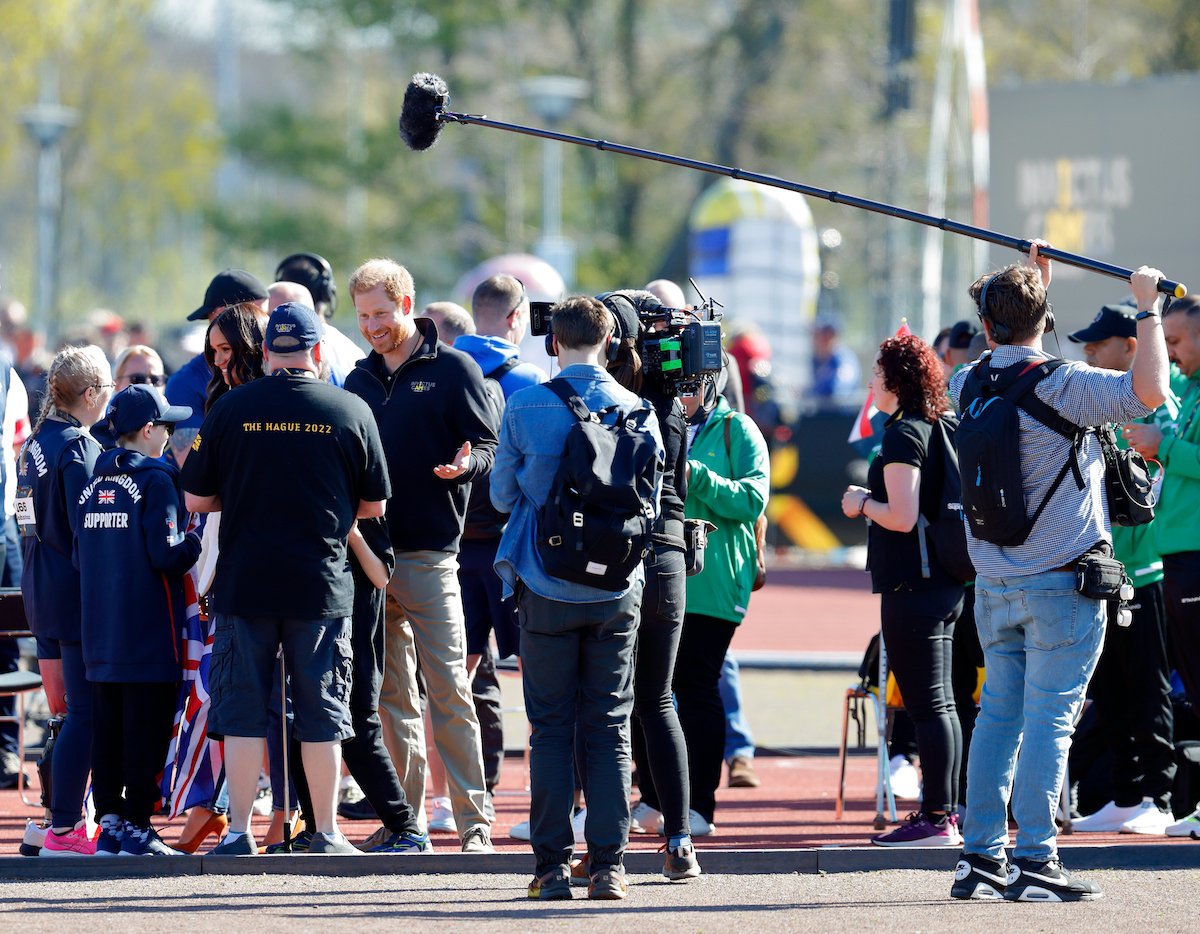 Meghan Markle and Prince Harry, who felt differently about 'creating content' such as their Netflix 'Harry & Meghan' docuseries, according to a commentator, talk to people at the Invictus Games with a film crew in tow.