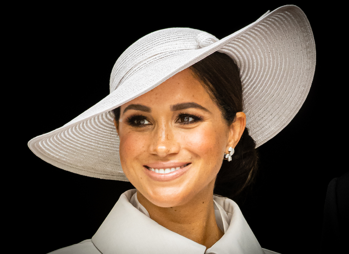 Meghan Markle, who is being slammed by haters for failing to acknowledge her "privilege," smiles in a white hat at an event.