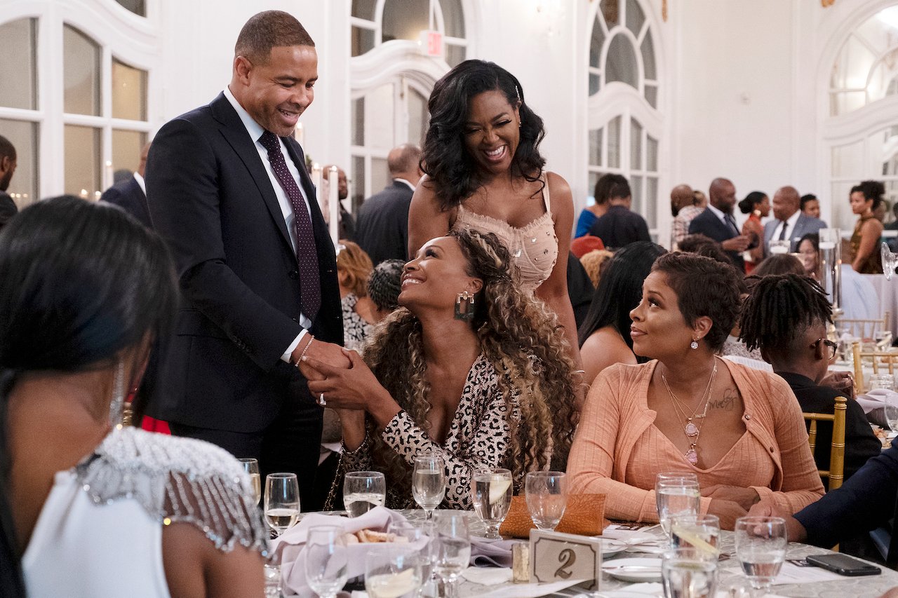 Mike Hill and Cynthia Bailey smile and hold hands in front of 'RHOA' cast members