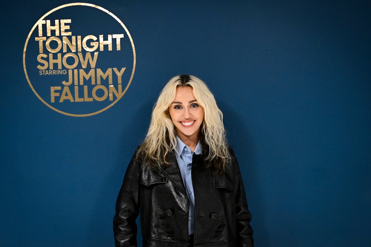 Miley Cyrus smiles and poses in front of a sign that says "The Tonight Show With Jimmy Fallon."
