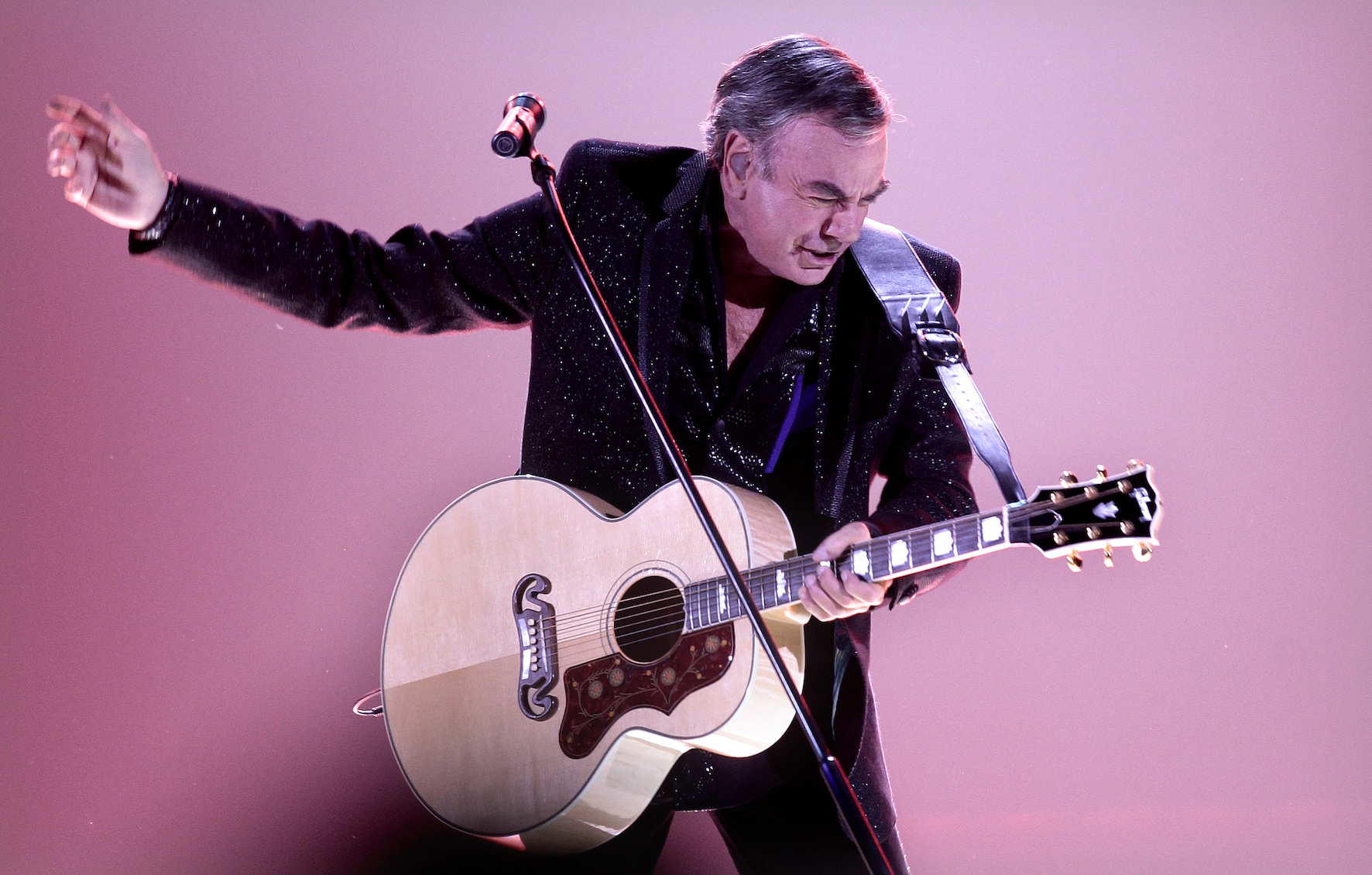Neil Diamond playing his guitar against a pink background