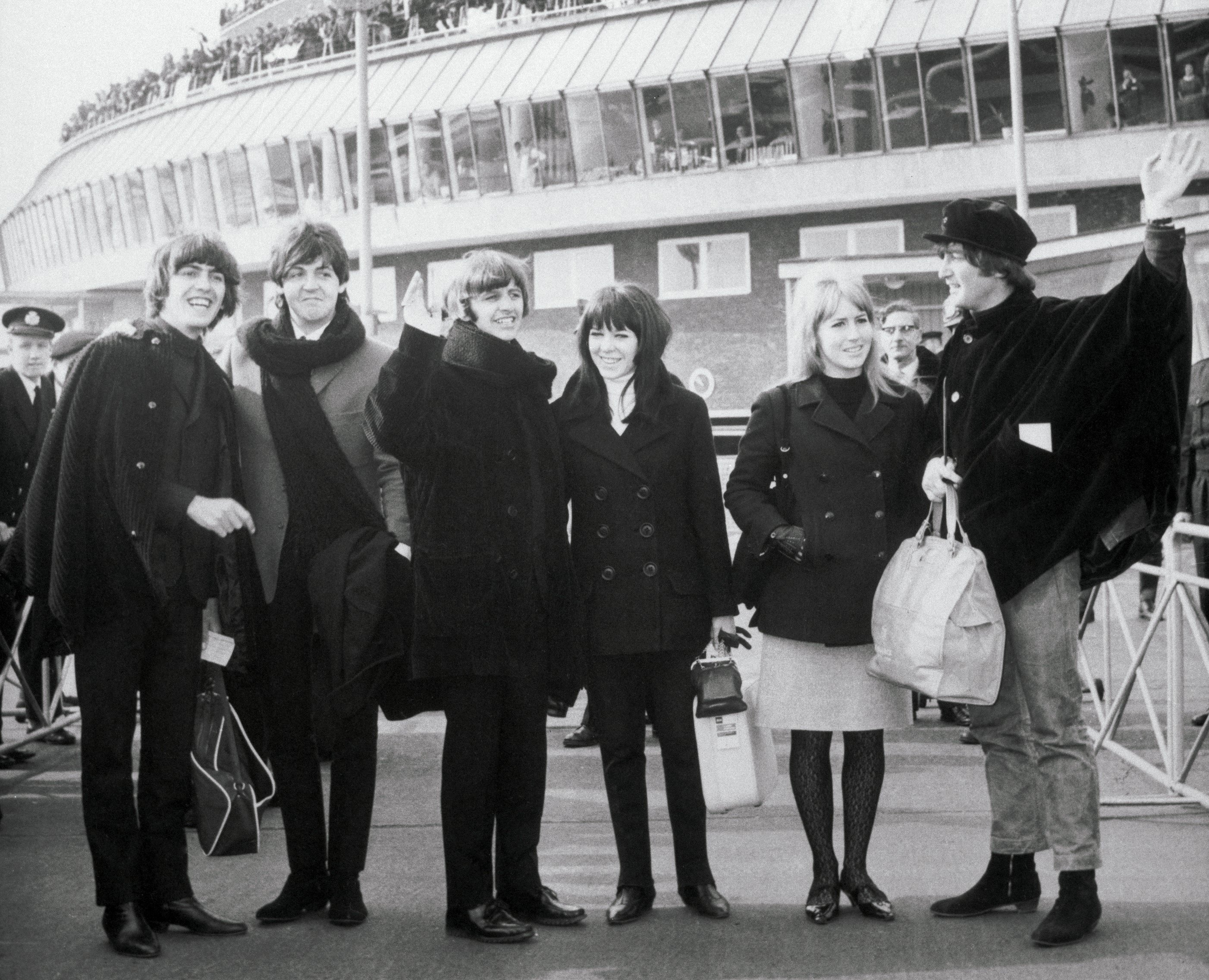 A black and white picture of George Harrison, Paul McCartney, Ringo Starr ,Maureen Starkey, Cynthia Lennon, and John Lennon at the airport.