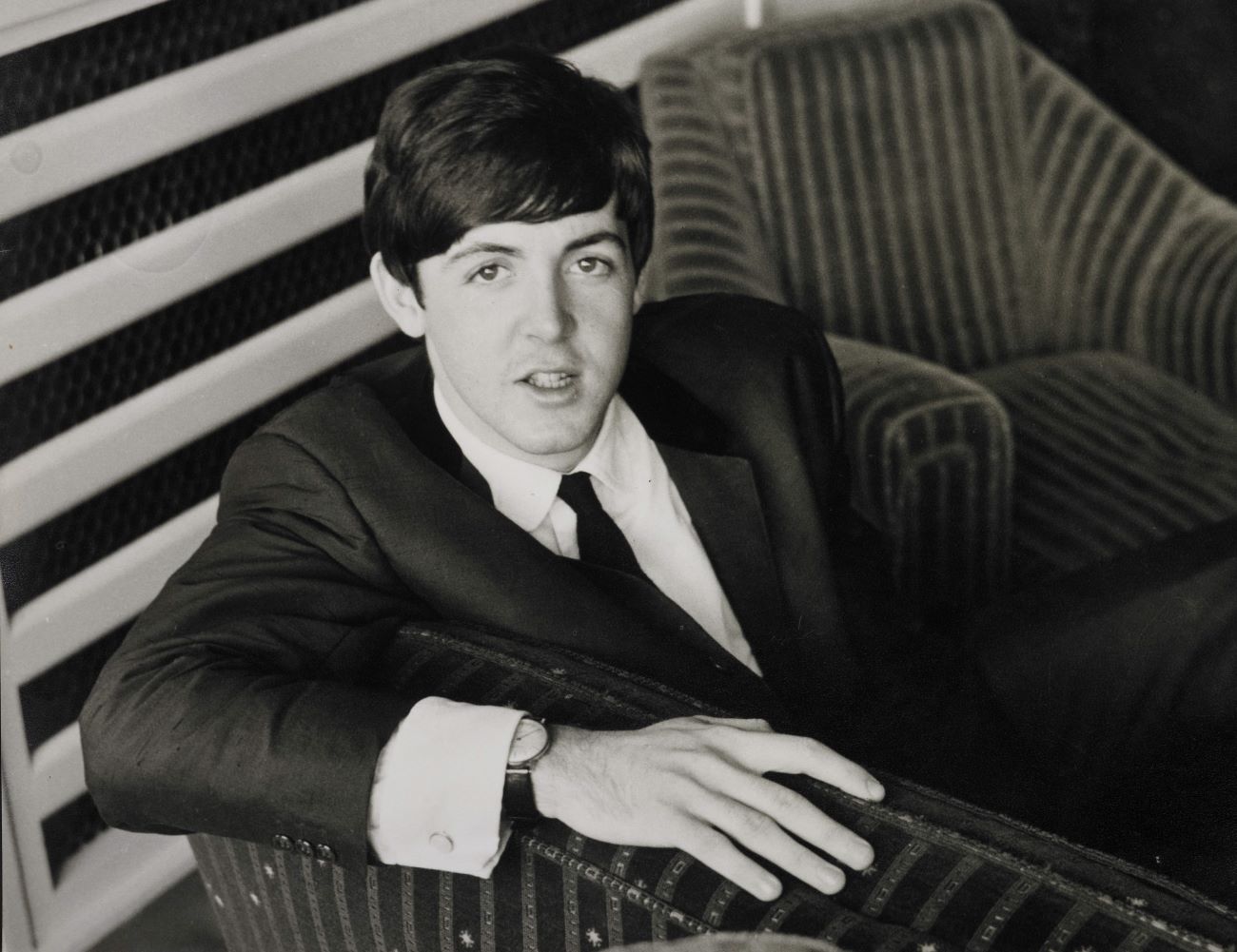 A black and white picture of musician and actor Paul McCartney wearing a suit and sitting in a chair.