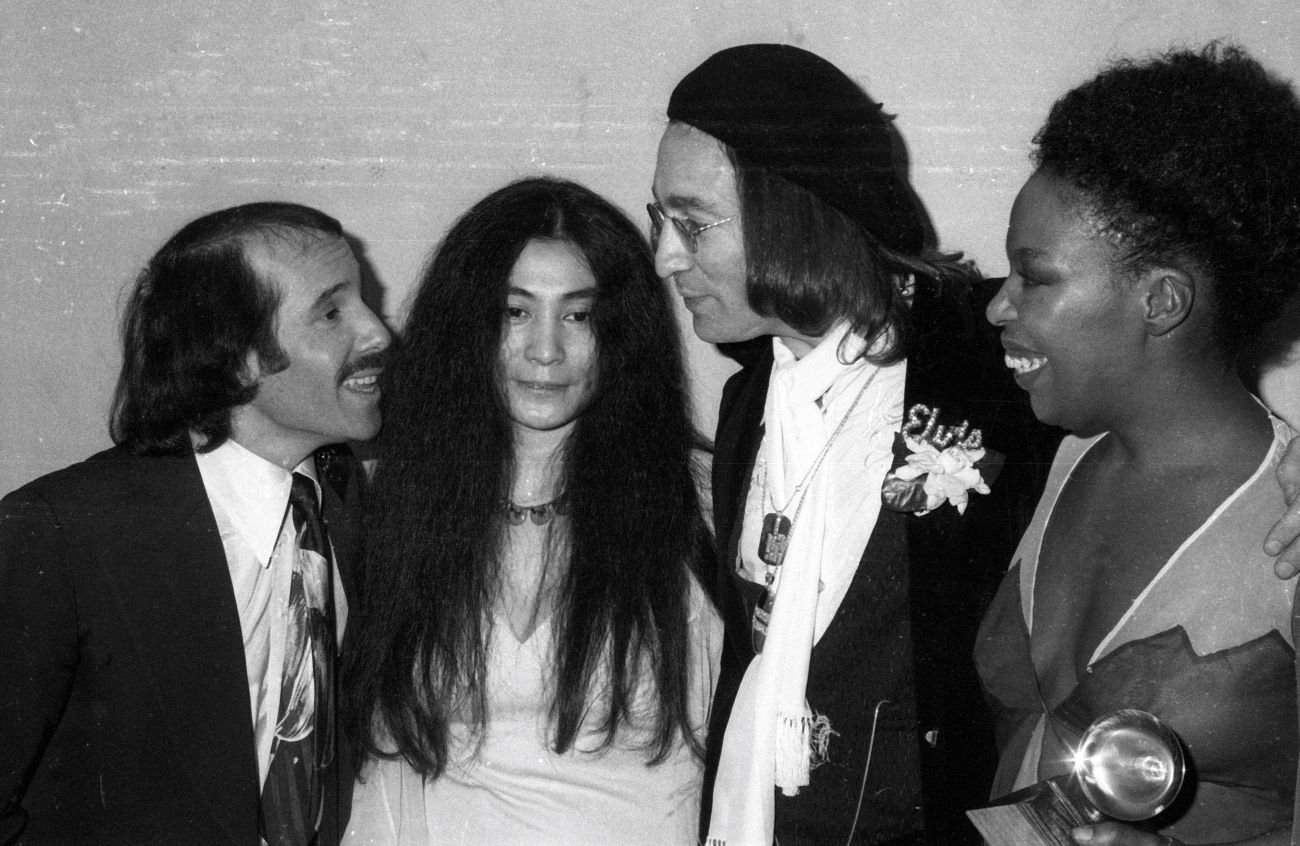 A black and white picture of Paul Simon, Yoko Ono, John Lennon, and Roberta Flack talking together.