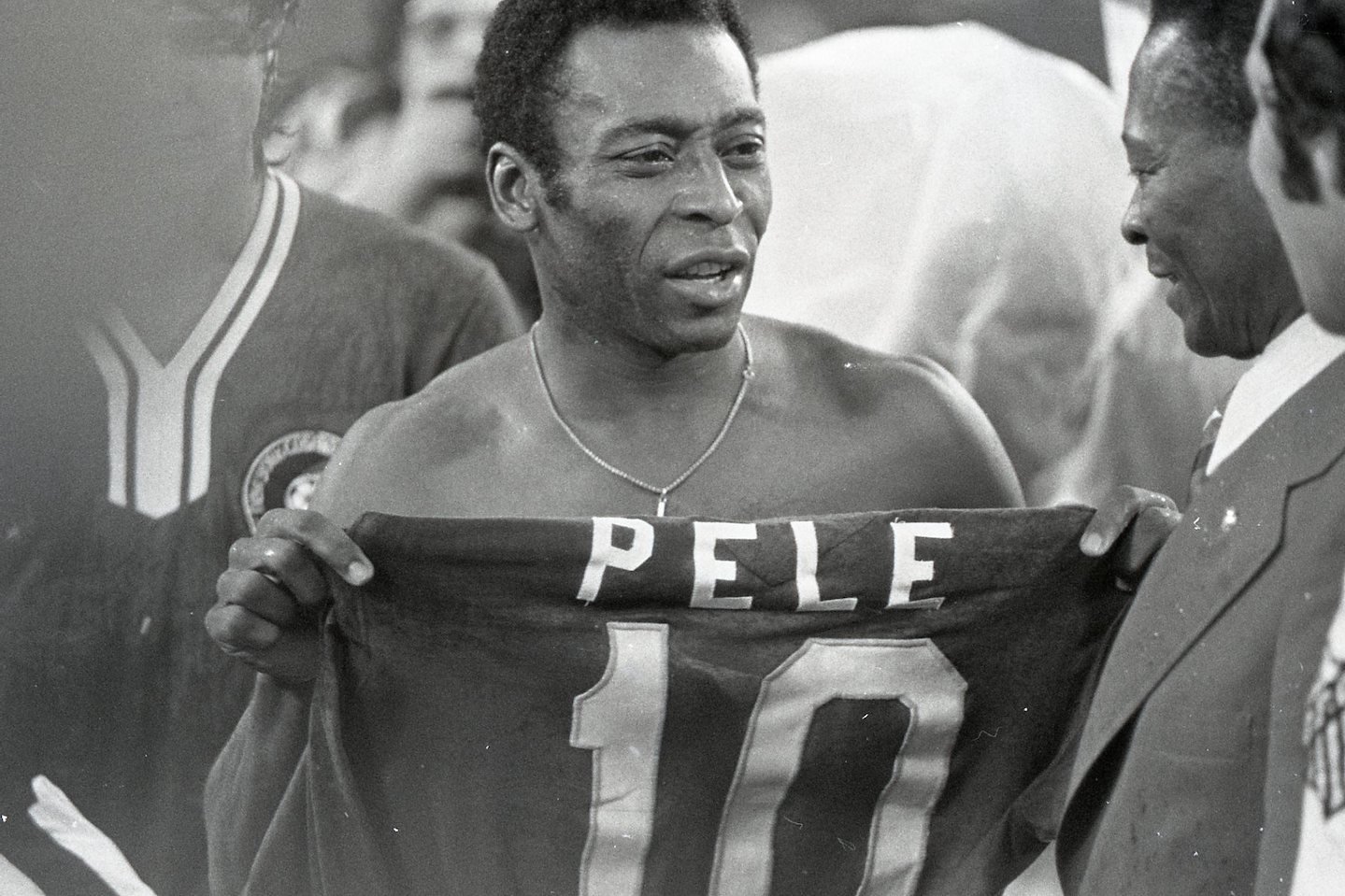 A black and white photo of Pelé holding his jersey up after a game