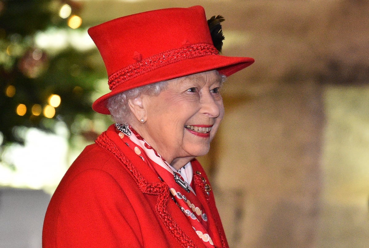 Queen Elizabeth II, who has a Christmas tree dedicated to her at Windsor Castle, smiles and looks on wearing a red coat and hat