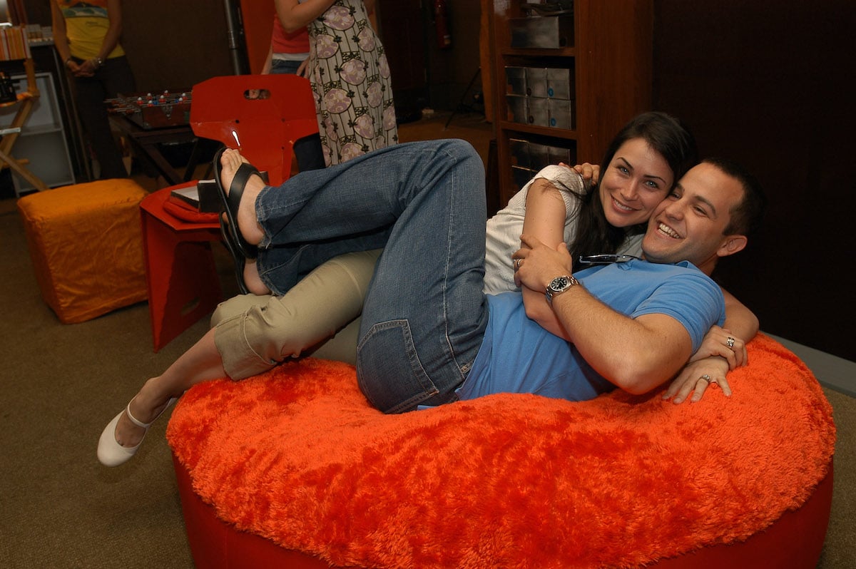 Rena Sofer and Sanford Bookstaver smiling, sitting on a large ottoman