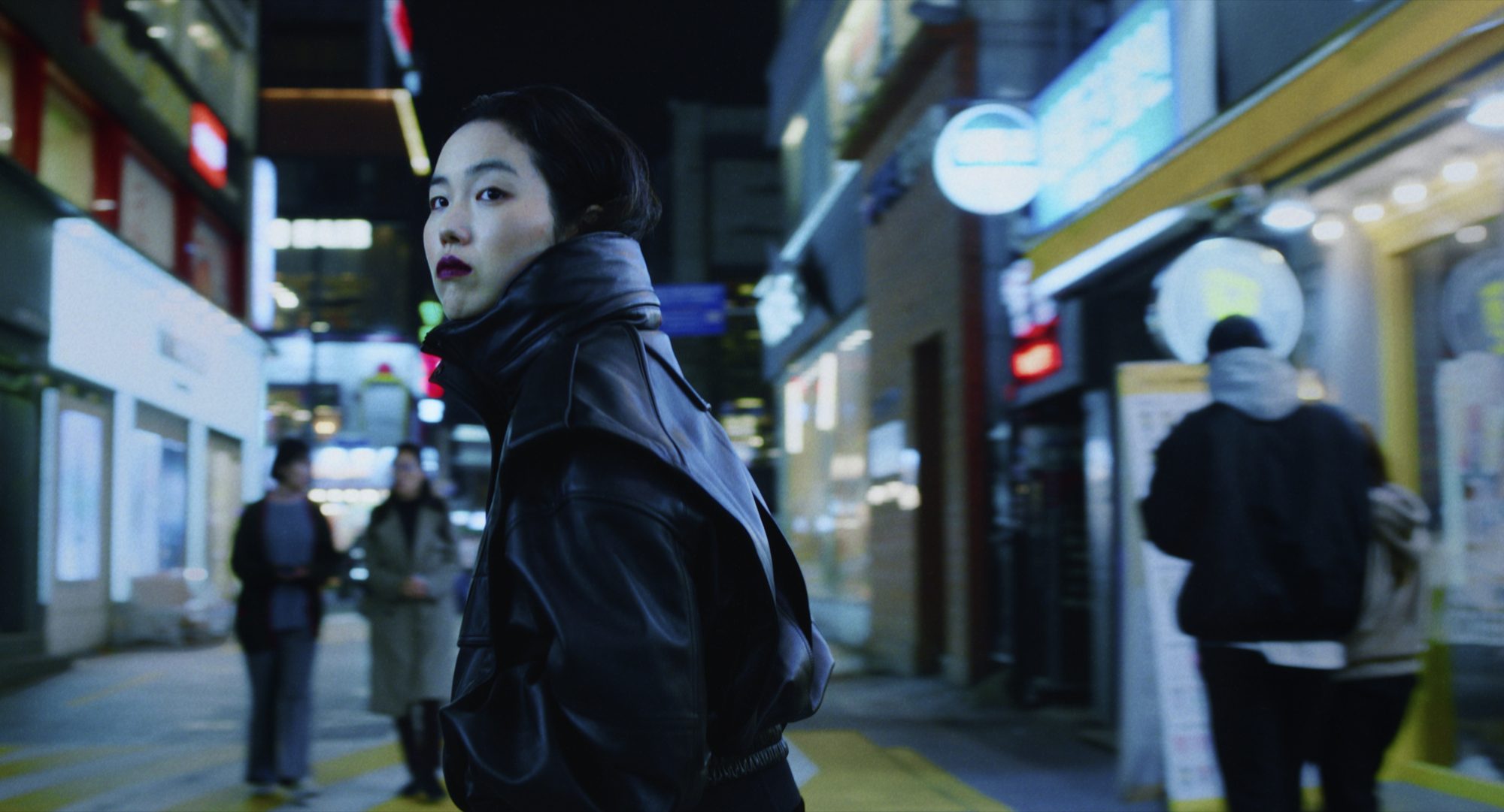 'Return to Seoul' Park Ji-Min as Frédérique Benoît AKA Freddie wearing a black leather jacket, looking over her shoulder on the street