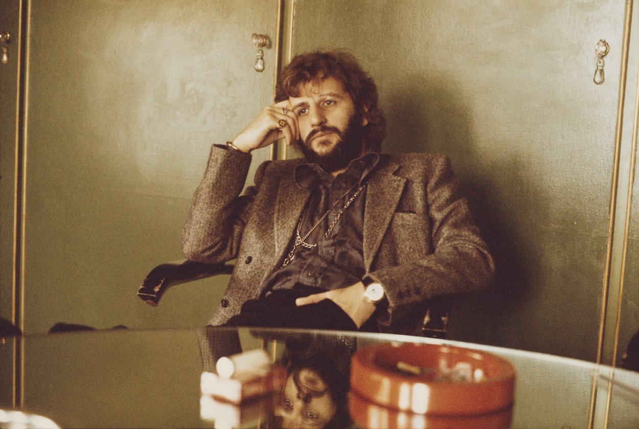 Ringo Starr wears a blazer while sitting in a London office in 1973 with cigarettes and ashtray within reach on a table.