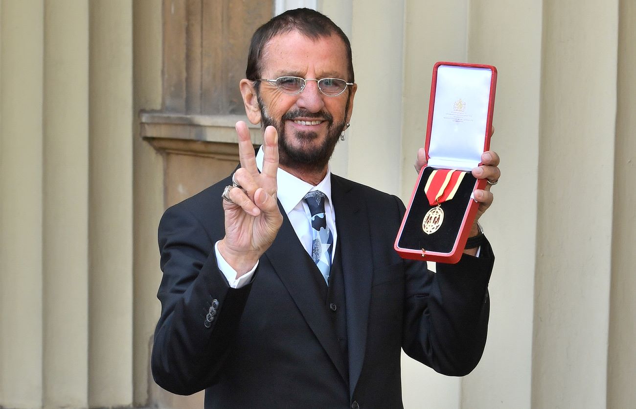 Ringo Starr holds a medal and holds up a peace sign after being knighted.