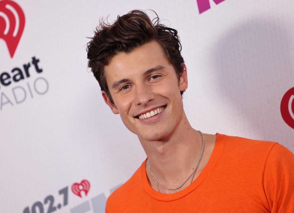 Shawn Mendes, who owns a penthouse condo in his hometown of Toronto, Canada, smiles and poses at an event in an orange shirt.