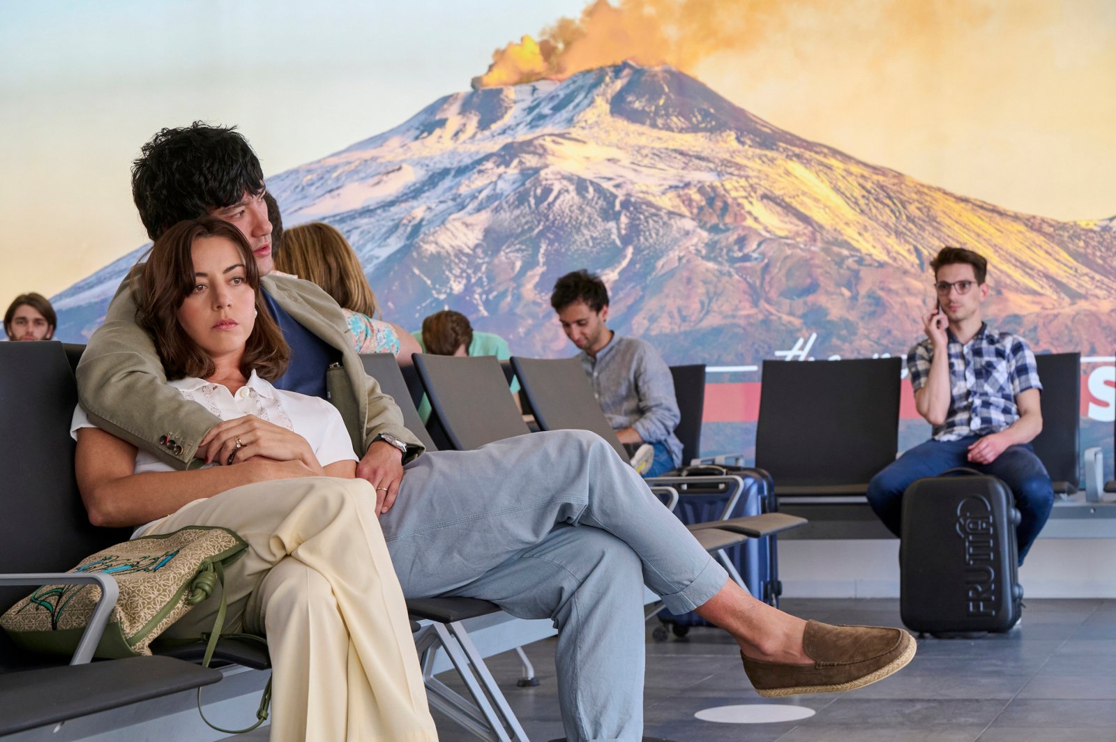 Aubrey Plaza and Will Sharpe in 'The White Lotus' Season 2 finale for our article about shows like it to watch before season 3. They're sitting in an airport, and he has his arm around her.