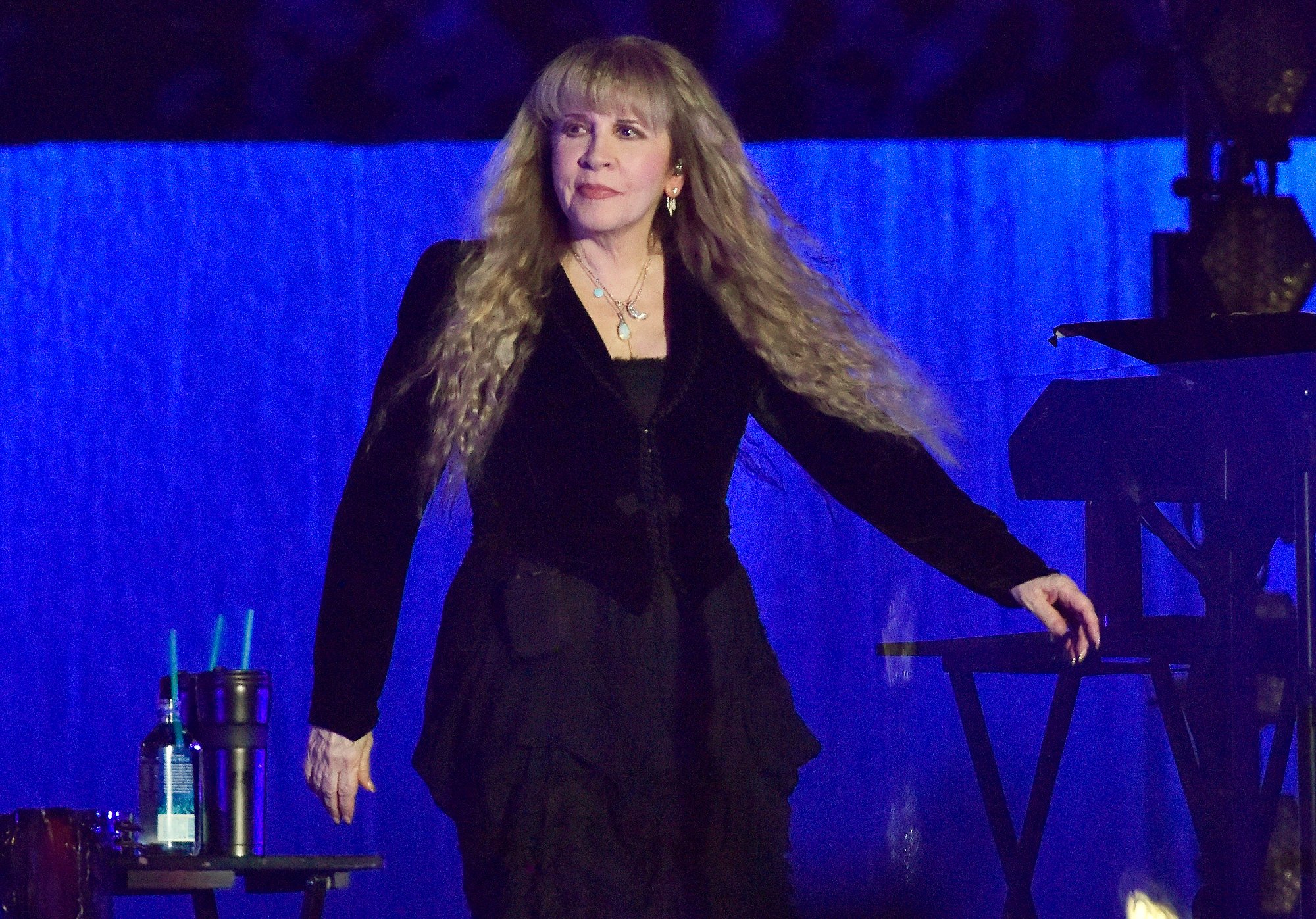 Stevie Nicks walks on stage wearing a black long-sleeved outfit