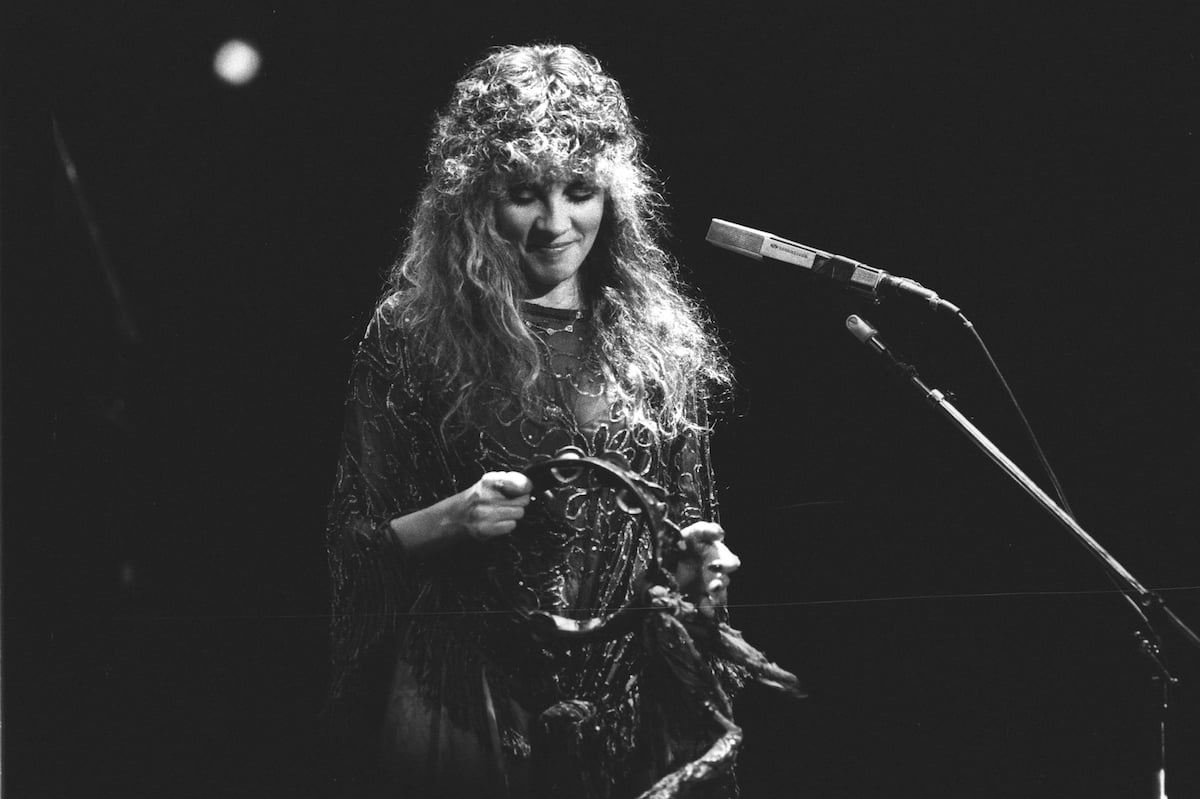 A black and white photo of Fleetwood Mac star Stevie Nicks holding a tambourine on stage.