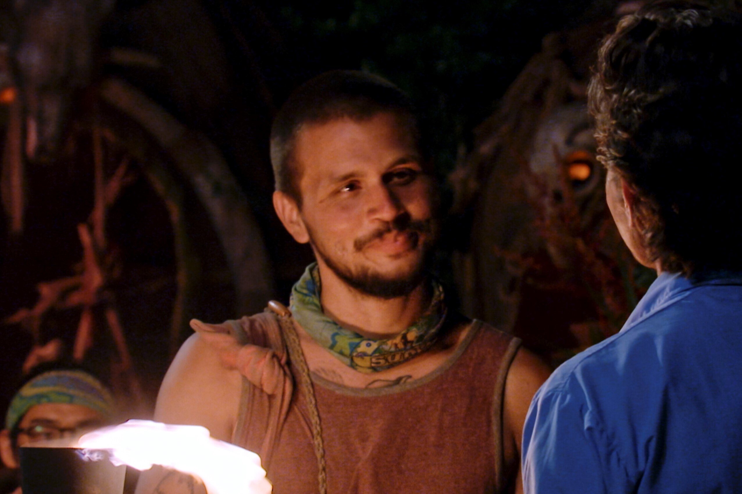 Jesse Lopez, who starred in 'Survivor' Season 43 on CBS, watches as host Jeff Probst is about to snuff his torch. Jesse wears a muted red tank top and light blue 'Survivor buff around his neck.