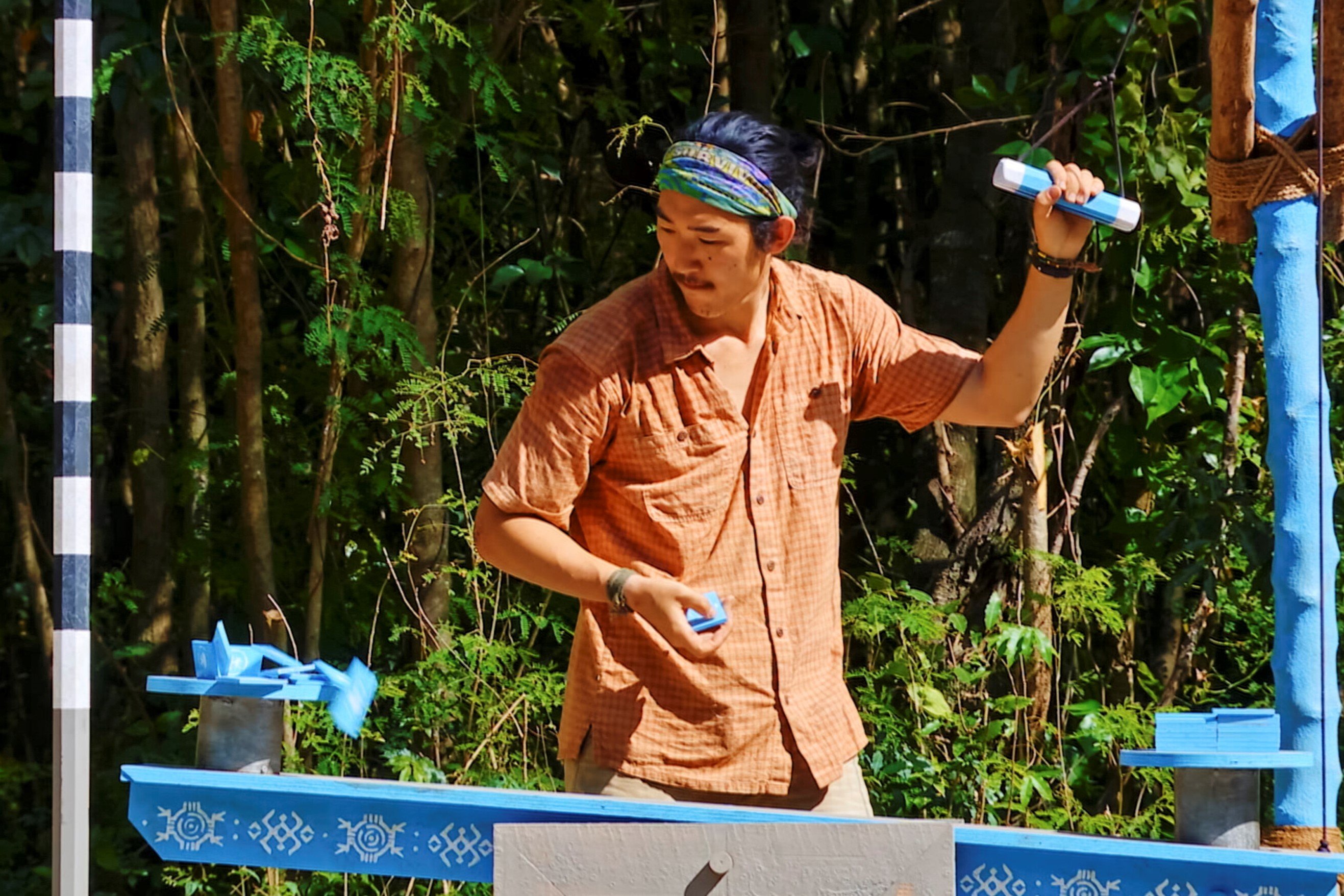 Owen Knight, who according to fans and spoilers, will make it to the Final Tribal Council in 'Survivor' Season 43 on CBS, competes in a challenge. Owen wears a short-sleeve orange button-up shirt, tan shorts, and his light blue 'Survivor' buff.