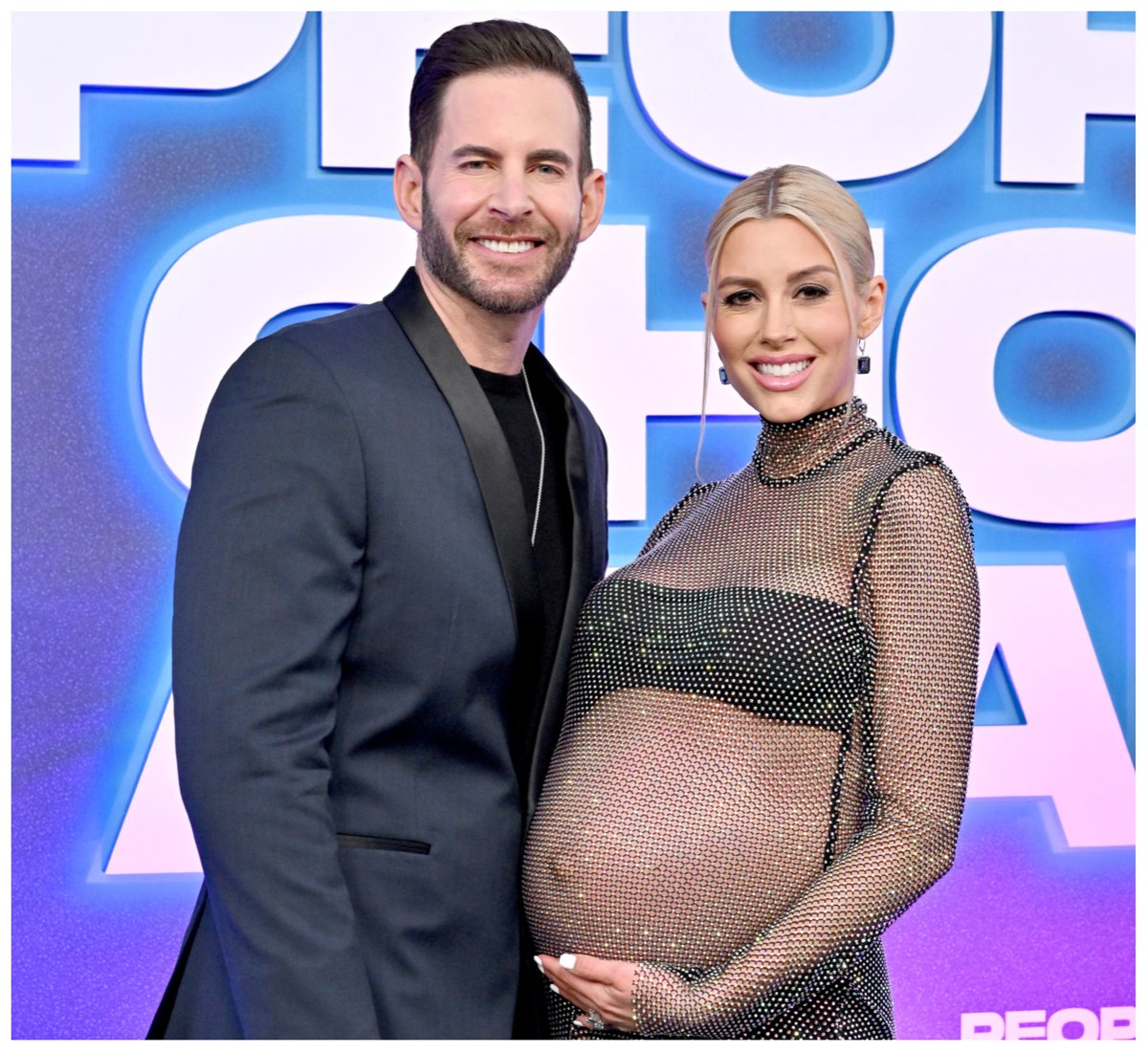 Tarek El Moussa and his pregnant wife, Heather Rae Young, smile and pose together at an event.