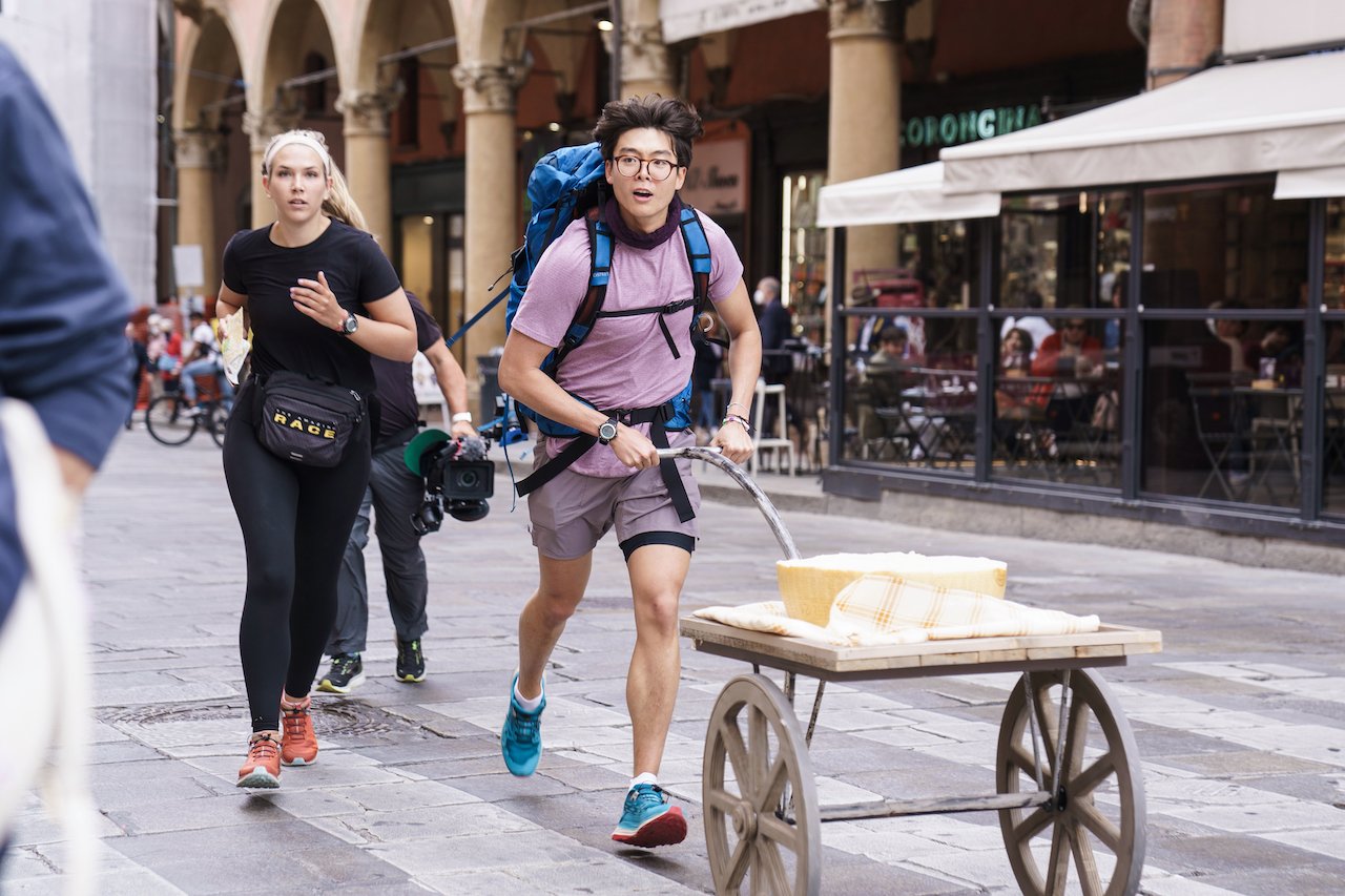 Claire Rehfuss runs next to Derek Xiao as he pushes a cart with a wheel of cheese on 'The Amazing Race 34'.