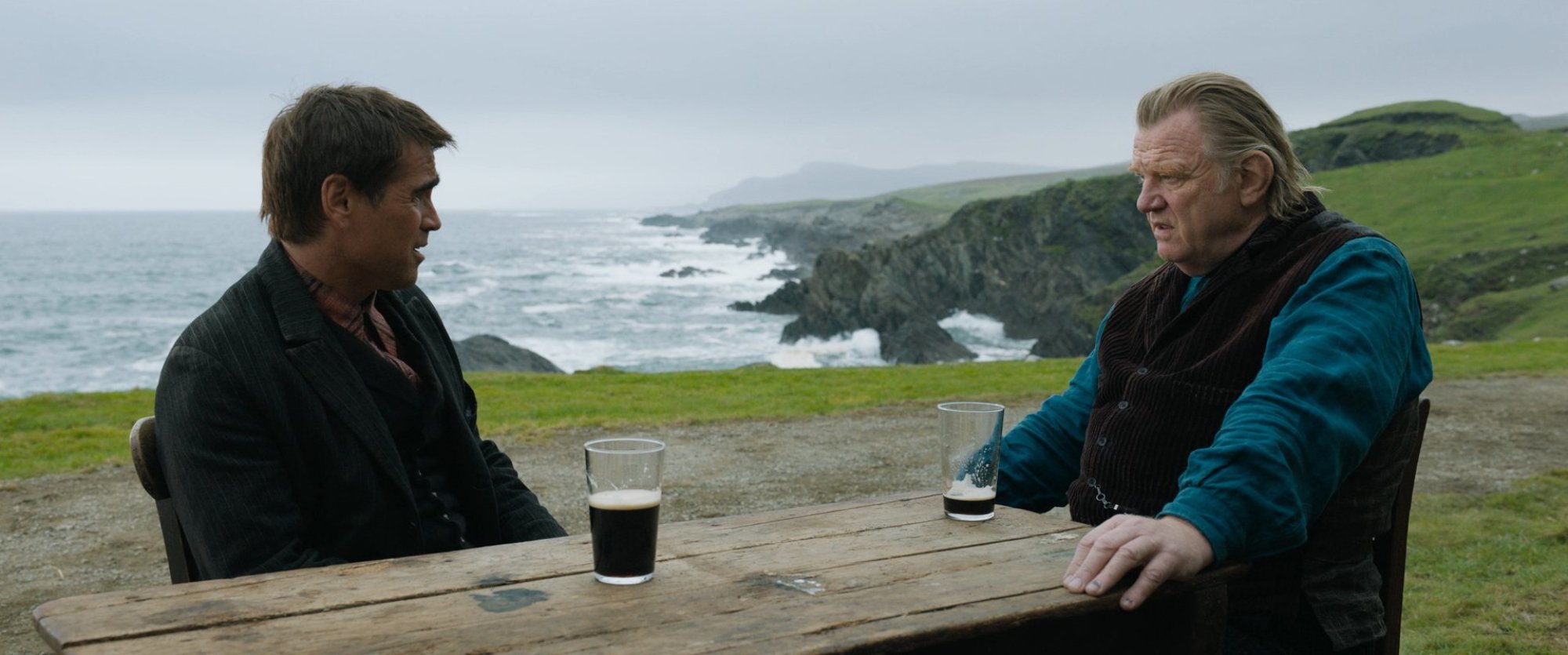 'The Banshees of Inisherin' Colin Farrell as Pádraic Súilleabháin and Brendan Gleeson as Colm Doherty sitting across from each other drinking beer in front of a view of the ocean
