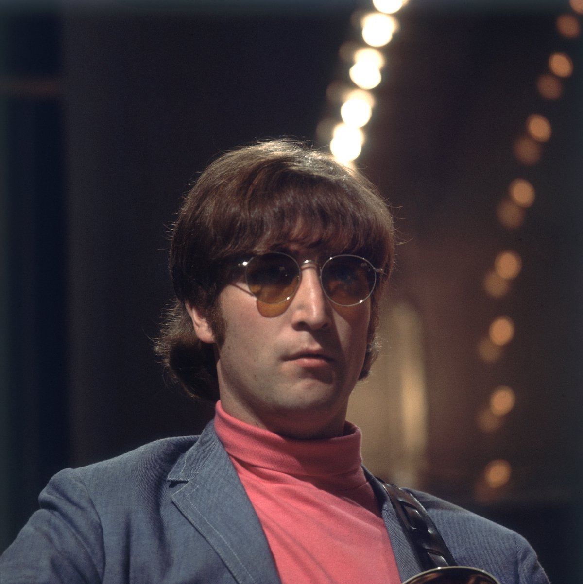 The Beatles' John Lennon wears sunglasses and his guitar strapped to his shoulder