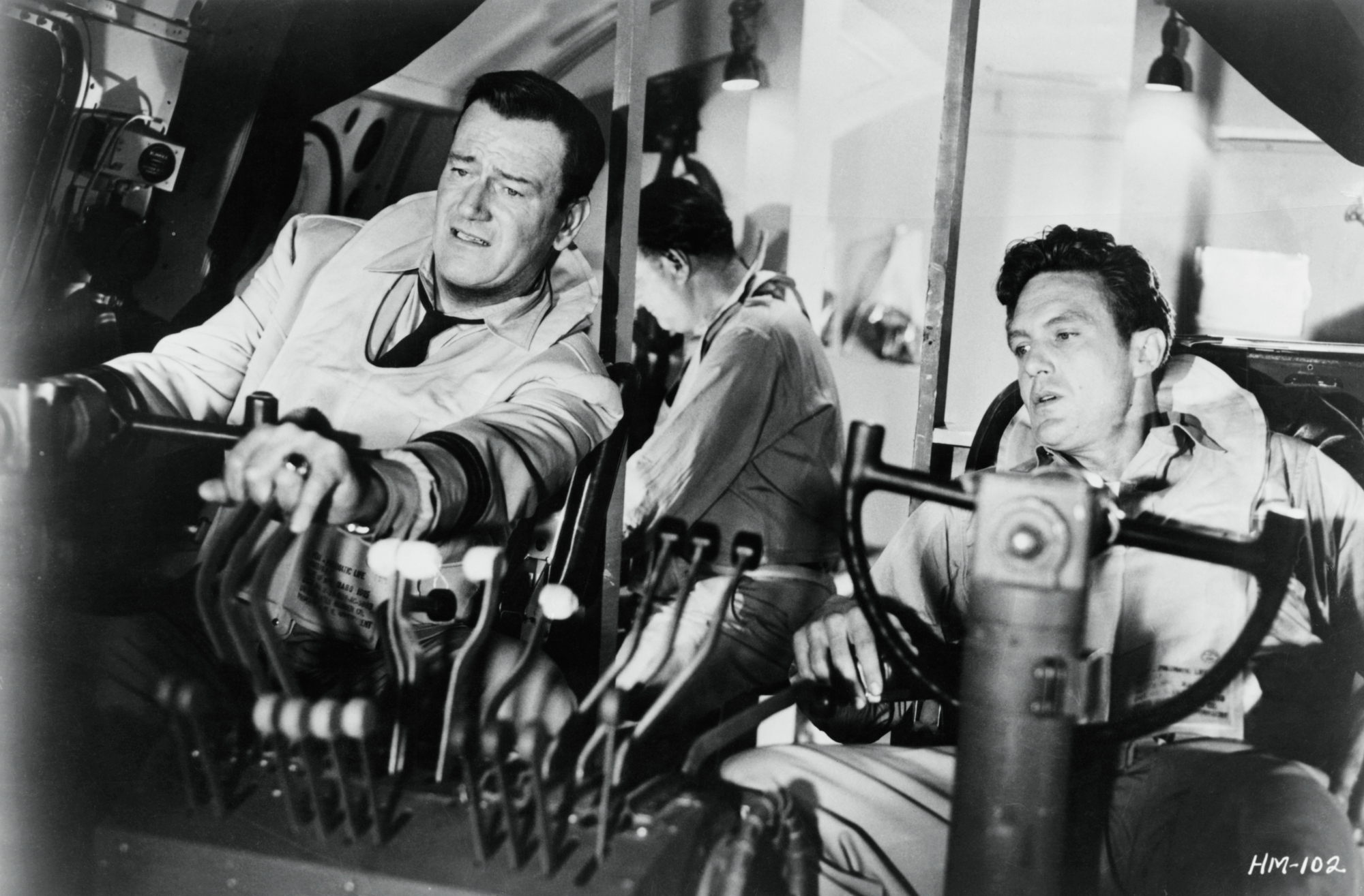 'The High and the Mighty' John Wayne as Dan Roman and Robert Stack as John Sullivan in movie roles. Black-and-white picture showing them sitting at the controls.