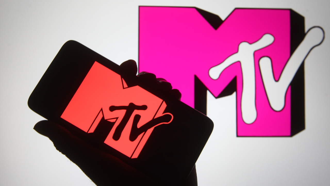 In this photo illustration a silhouette hand is seen holding a smartphone with MTV channel logo on a its screen