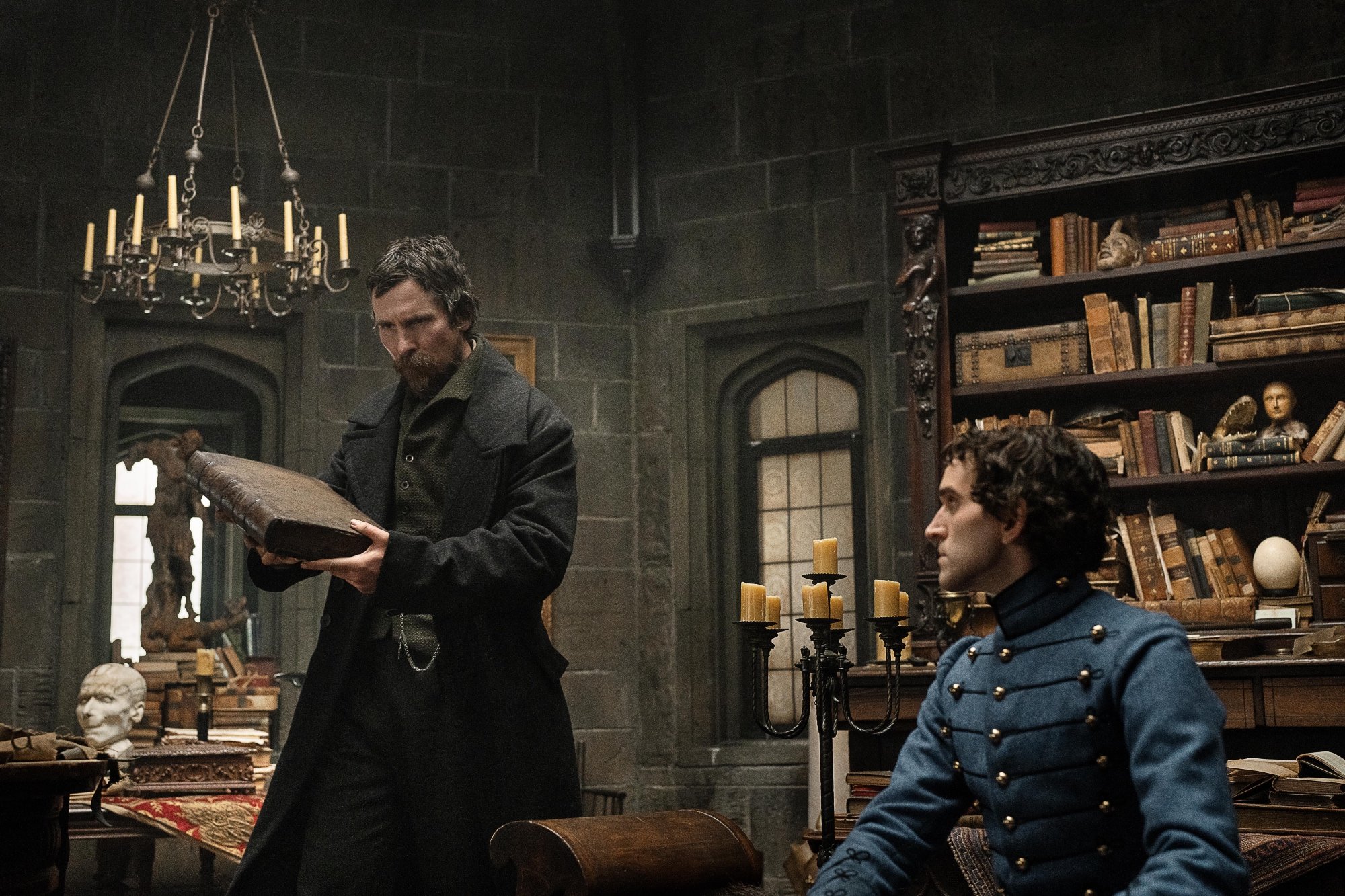 'The Pale Blue Eye' Christian Bale as Augustus Landor and Harry Melling as Edgar Allen Poe looking at a large brown book inside of a study