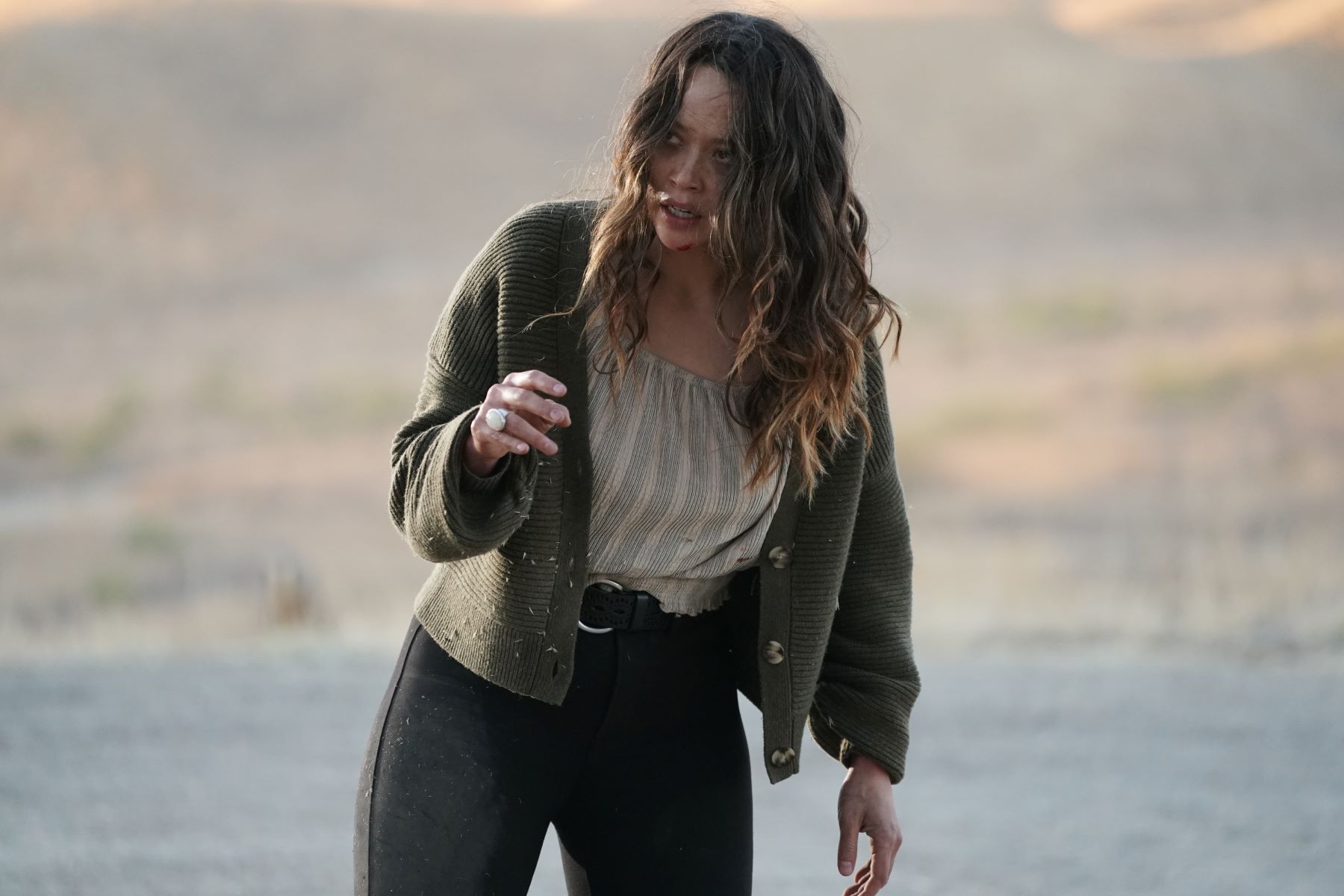 Melissa O'Neil, in character as Lucy Chen in 'The Rookie' on ABC, films a scene where she was captured by a man working with Rosalind Dyer, who apparently died in season 5. Lucy wears a dark green cardigan over a white top and black pants.