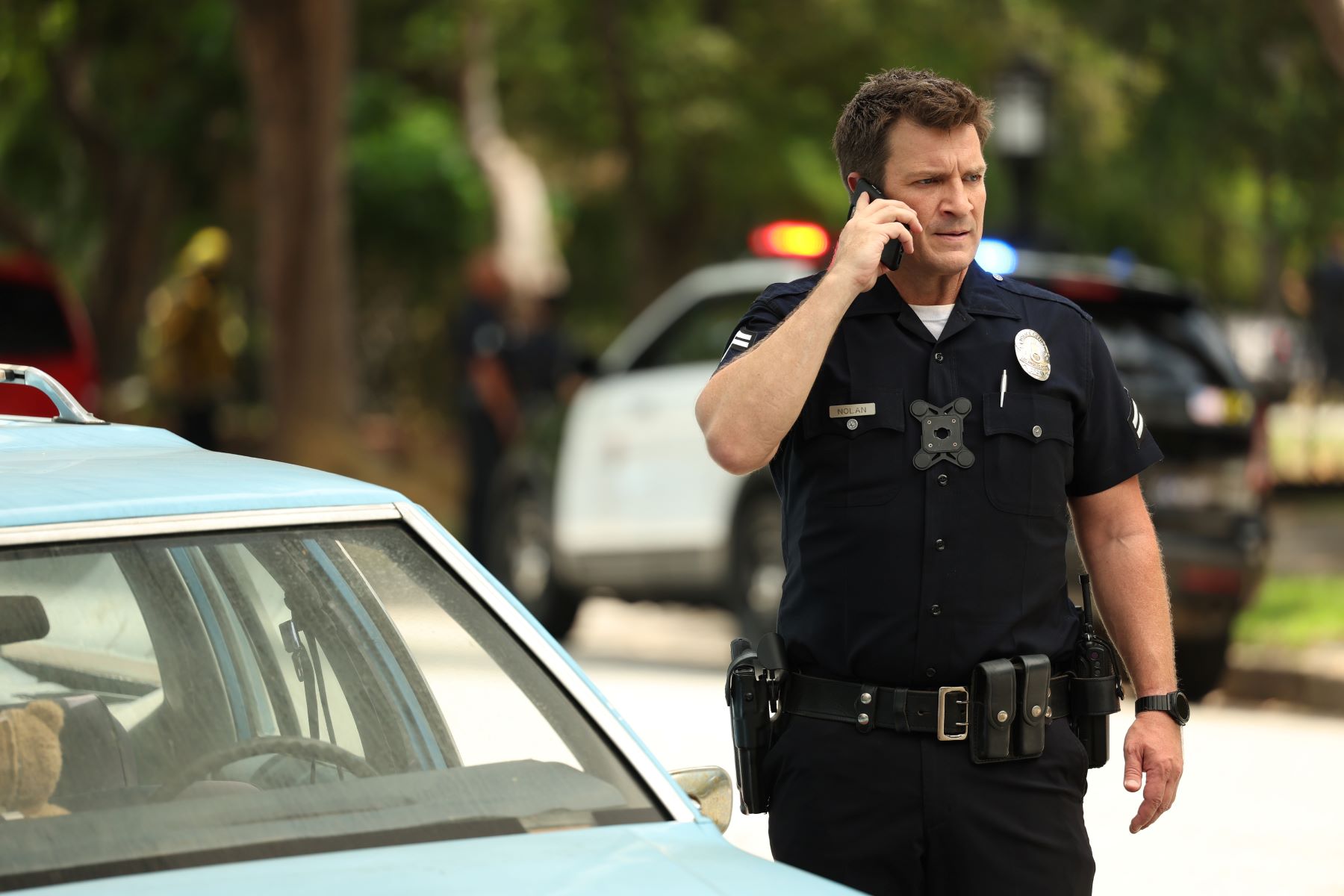 Nathan Fillion, in character as John Nolan in 'The Rookie' Season 5 on ABC, wears his dark blue police uniform while holding his cell phone up to his ear.