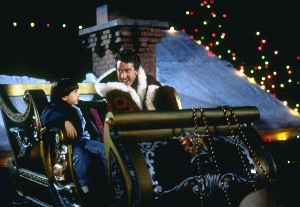 Eric Lloyd as Charlie and Tim Allen as Scott in the first 'The Santa Clause' movie in 1994. The father and son sit in Santa's sleigh on a roof.