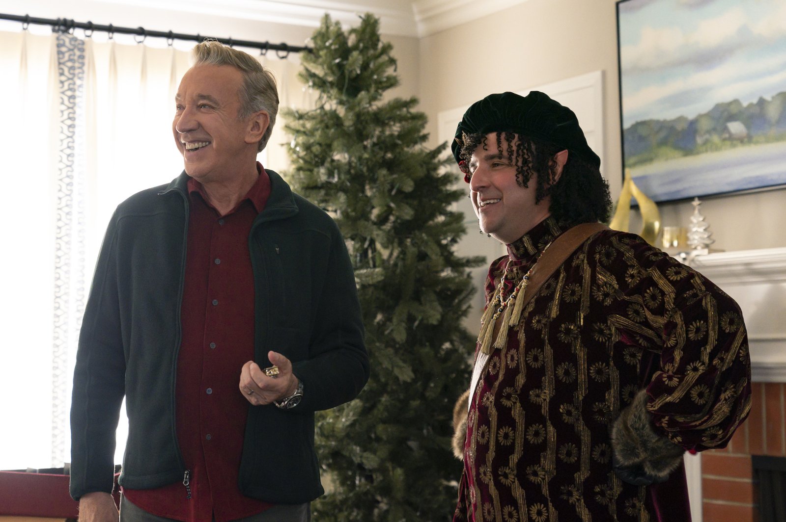 Tim Allen and David Krumholtz as Scott Calvin and Bernard in 'The Santa Clauses' for our preview of the finale, episode 6. They're standing in front of a Christmas tree and smiling.