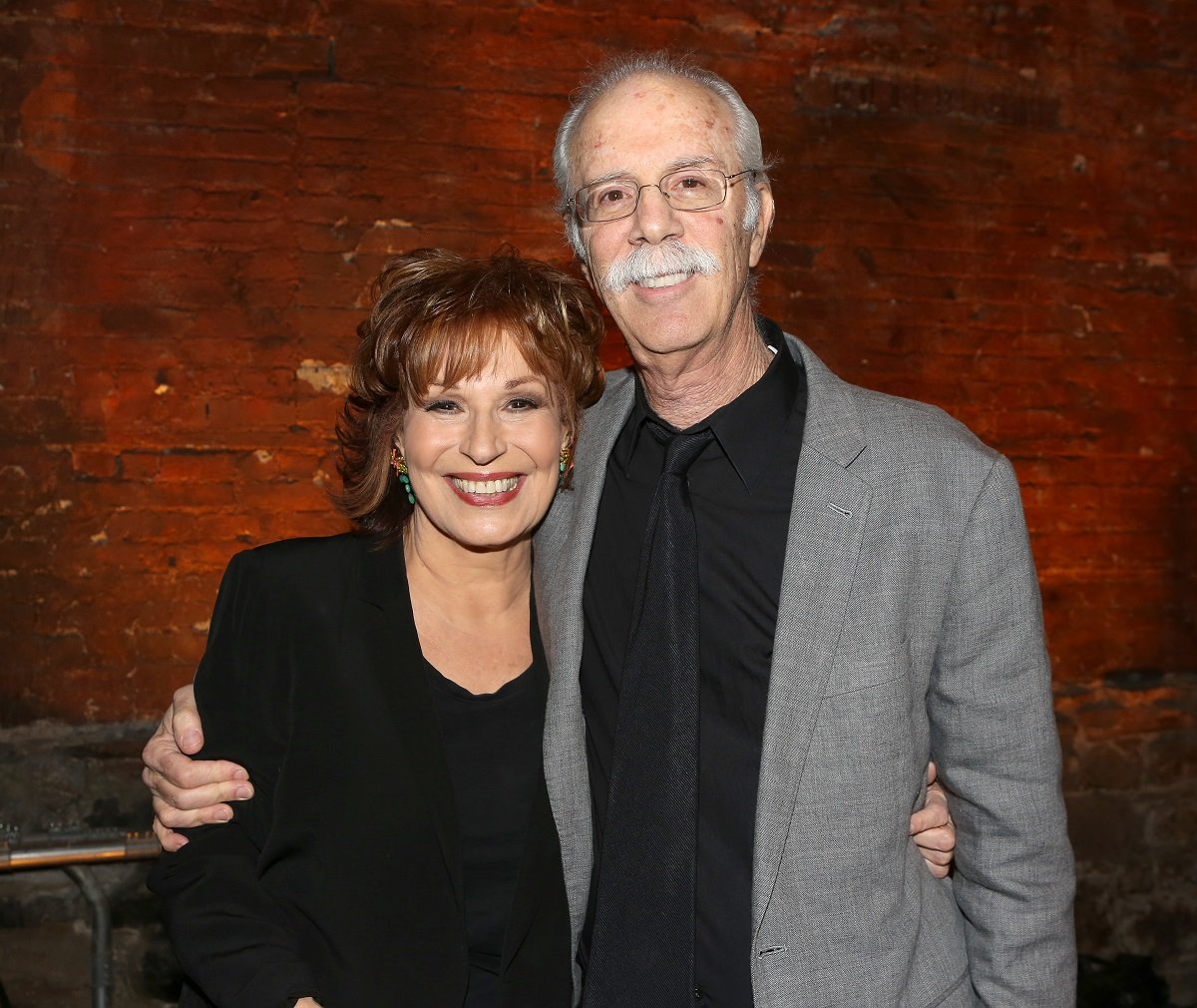 'The View' host Joy Behar in black, and her husband Steve Janowitz in a grey suit; smile for a photo.