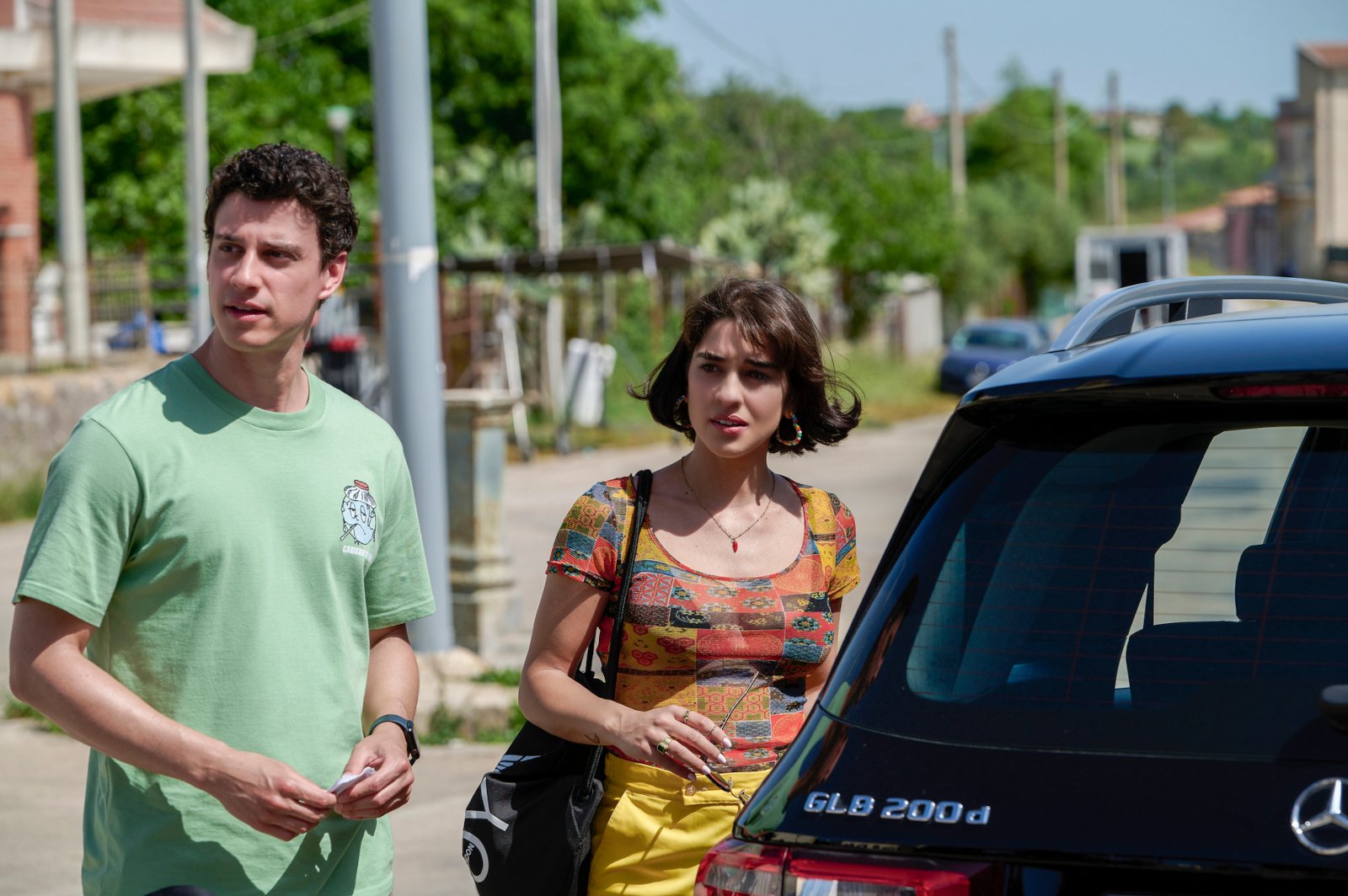 Adam DiMarco and Simona Tabasco in 'The White Lotus' Season 2 Episode 6. They're standing next to a car and staring at something off-screen.