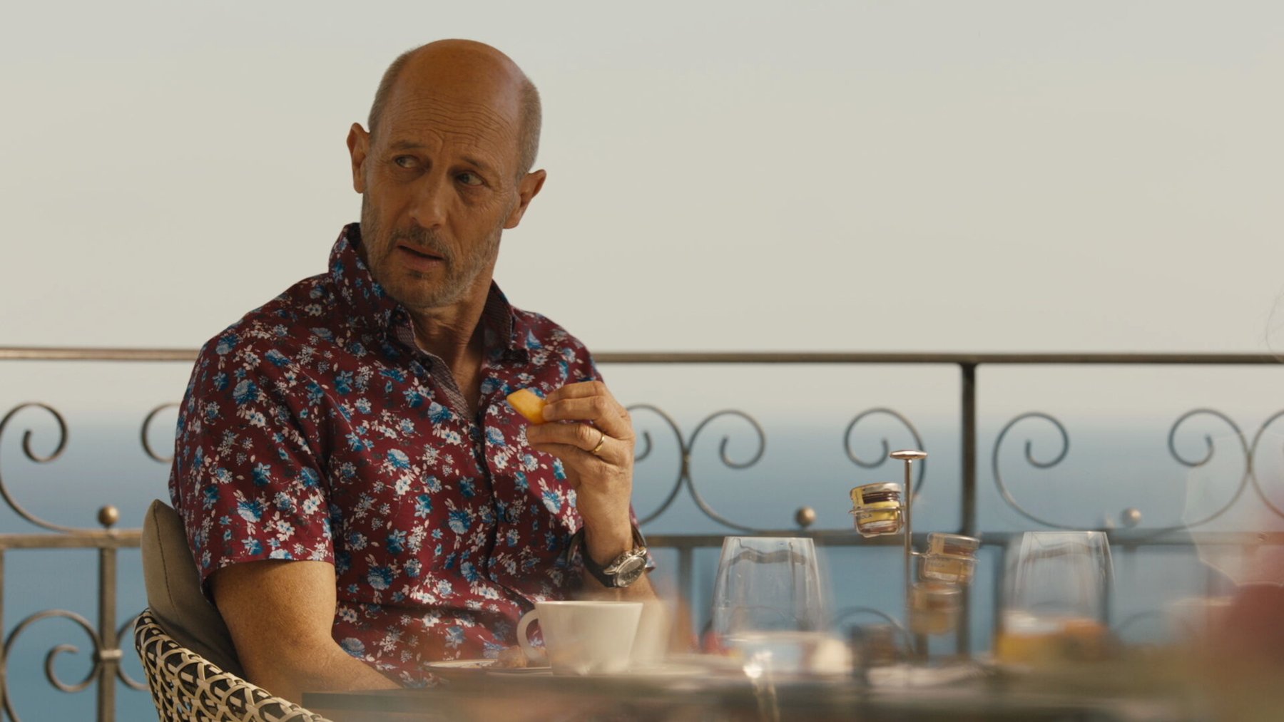Jon Gries as Greg in 'The White Lotus' Season 2. He's sitting at a table, holding a drink, and looking to the side of him.